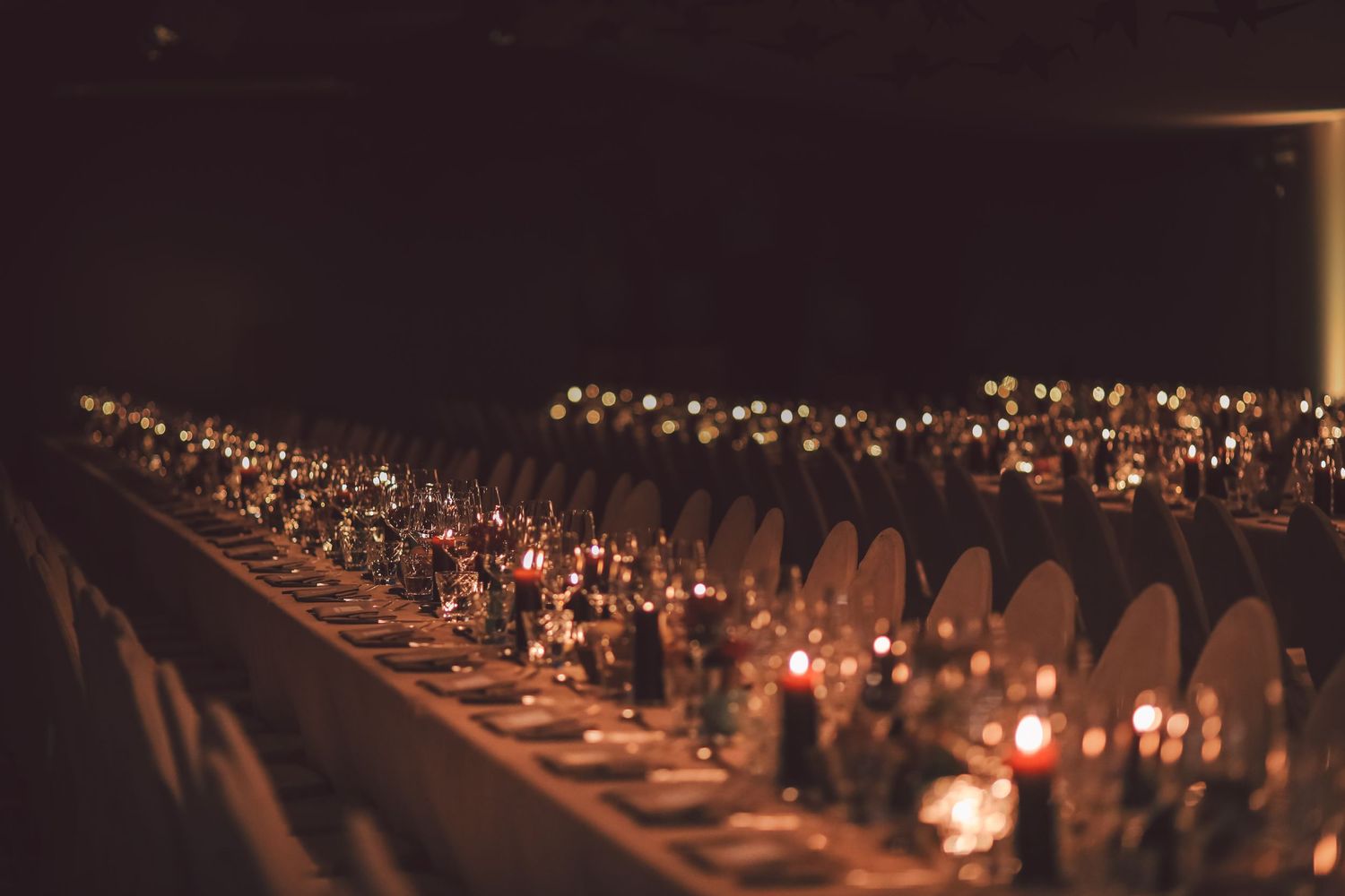 Long dining table set for an elegant candlelit dinner with romantic ambient lighting.