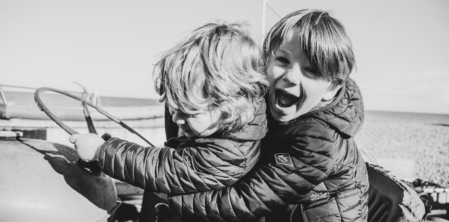 Black and white candid photo of two children laughing and hugging outdoors.
Family photography, Norfolk coast