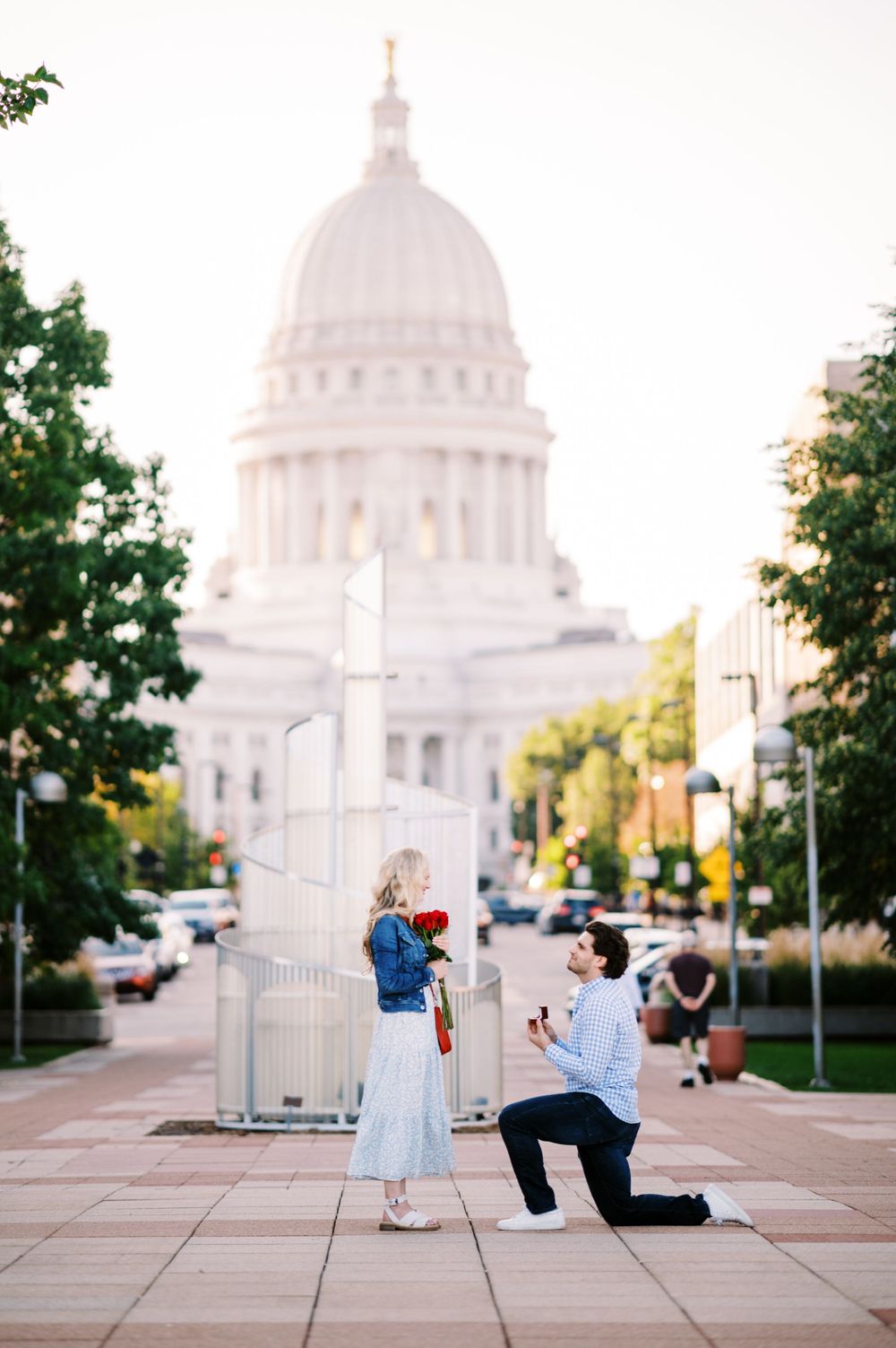A romantic proposal moment captured in front of the majestic Wisconsin State Capitol building in Madison at sunset.