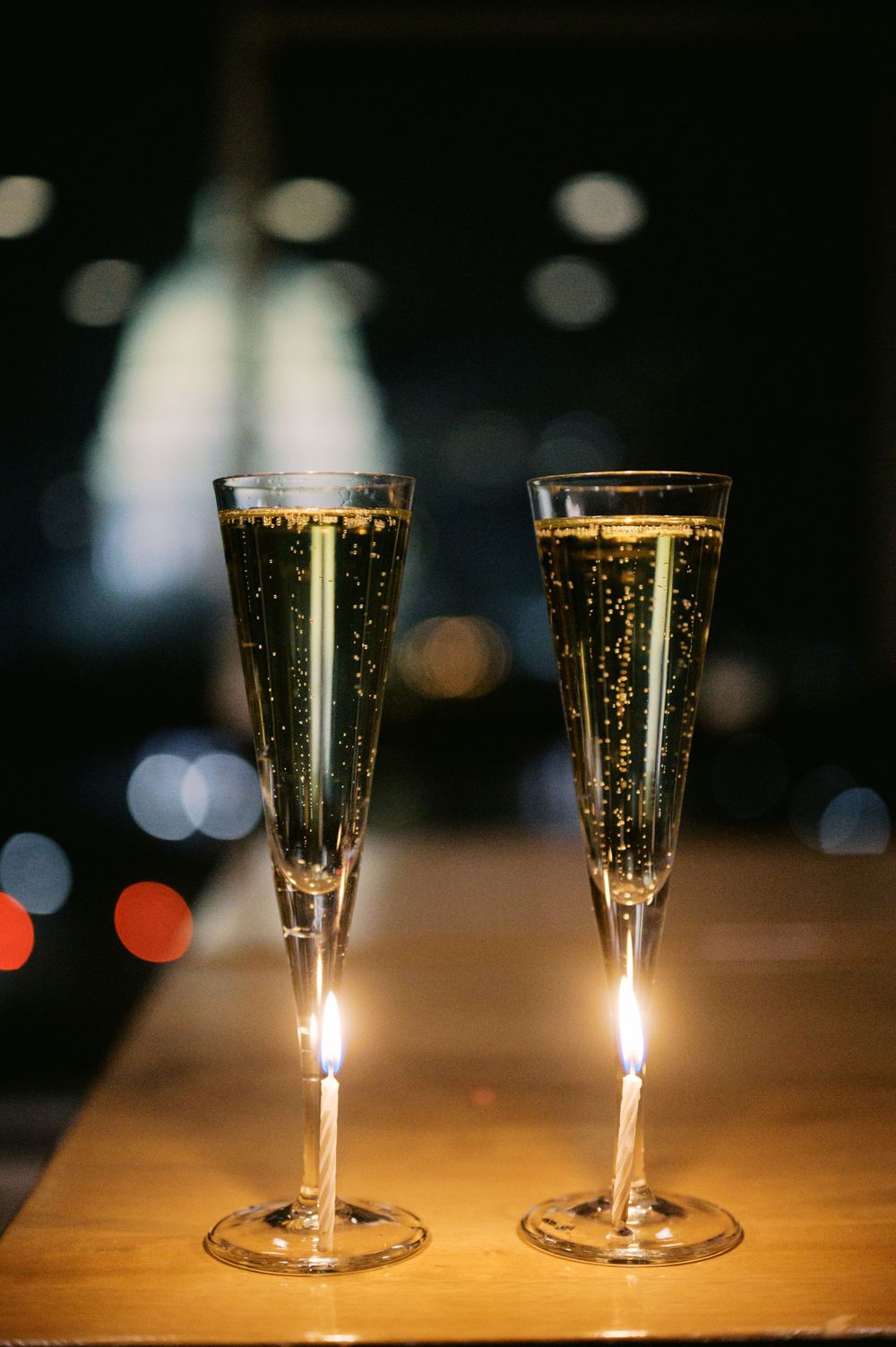 Two elegant champagne flutes filled with sparkling wine on a wooden table with bokeh lights in the background.