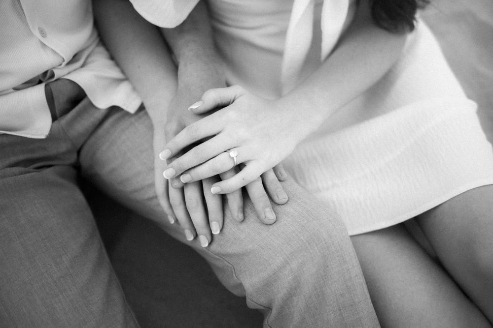 A close up black and white photo of hands gently resting together on light colored fabric.
