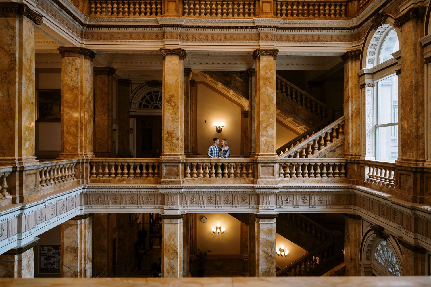Elegant marble staircase and balconies in a historic palace illuminated by warm wall sconces and natural light.