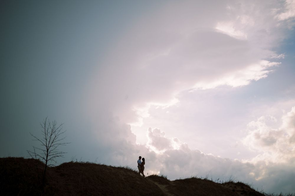 A silhouetted figure stands on a hilltop against dramatic cloudy skies with a bare tree in the background.