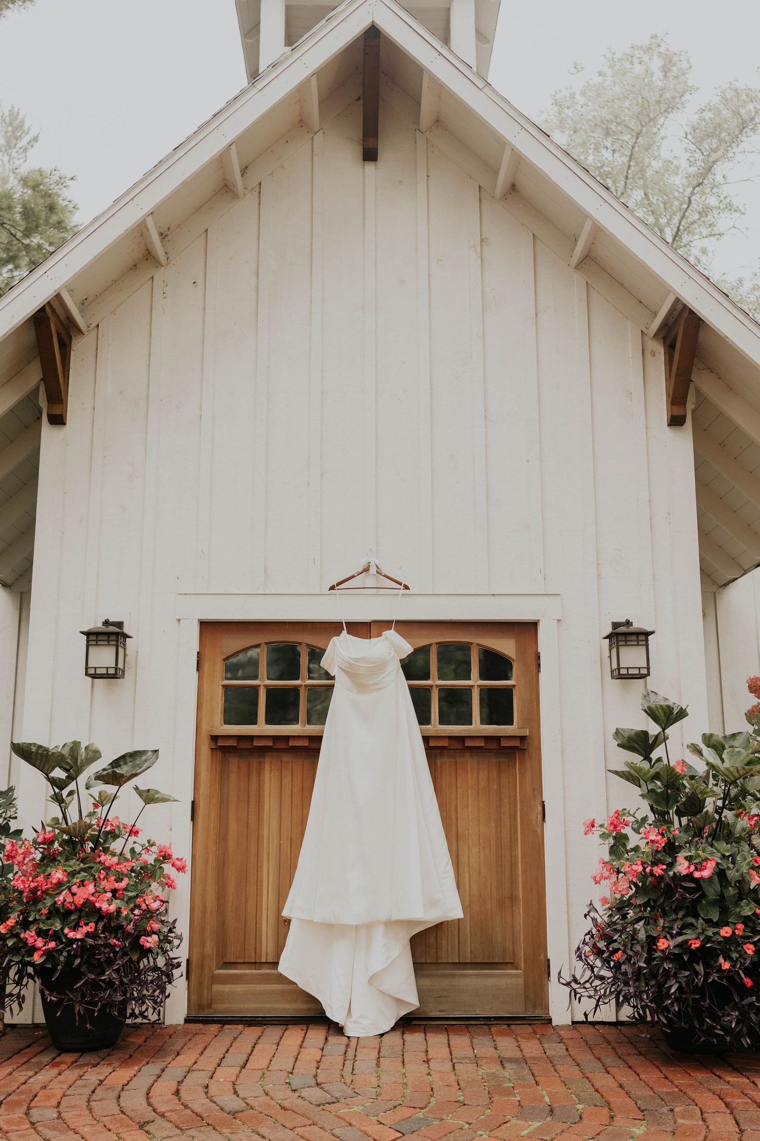 Elegant off-shoulder white wedding gown on marble stairs with matching white heels and small bouquet.