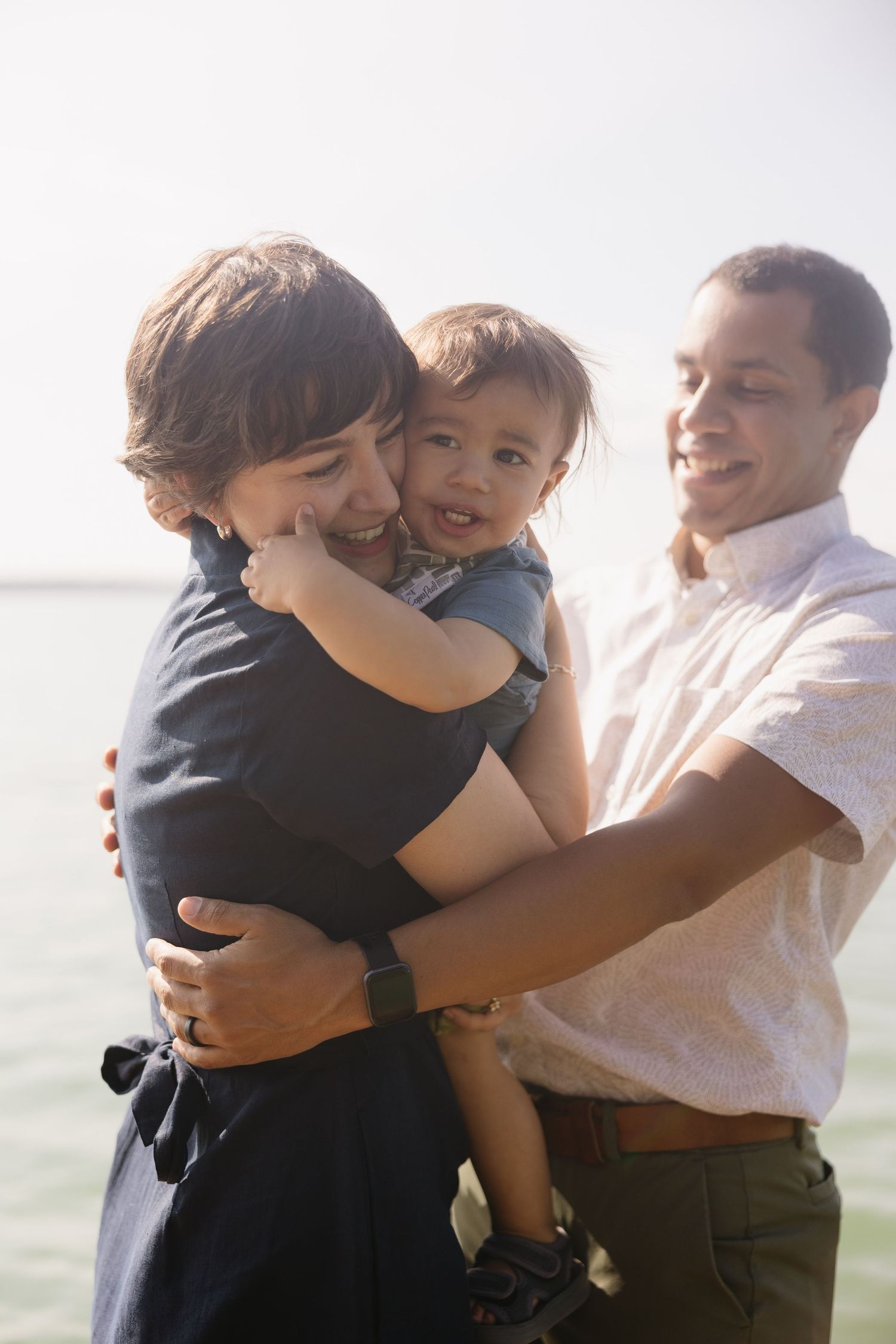 A joyful family embraces while sharing a tender moment by the water.