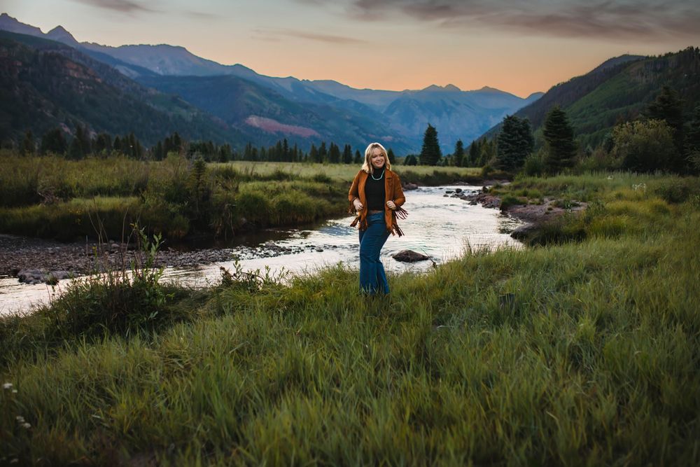 Person standing by mountain stream at sunset in picturesque valley setting.