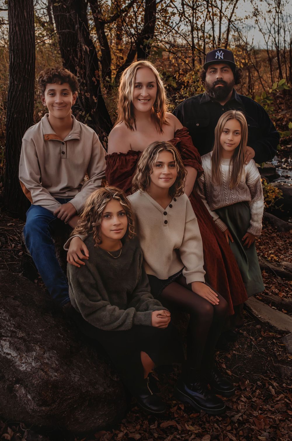 Family portrait of six people in earth tones against autumn forest background.