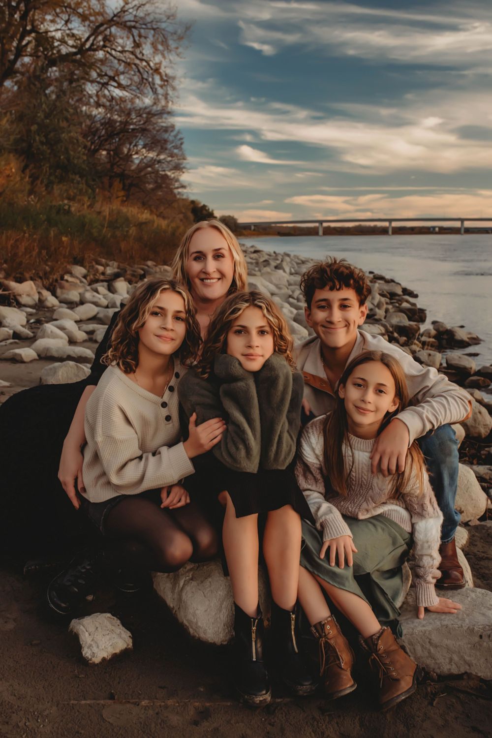 Group portrait of five people sitting together on rocky shoreline at sunset.