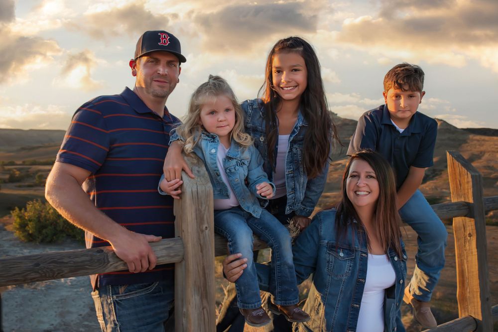 Family of five posing together at rustic wooden fence during sunset.