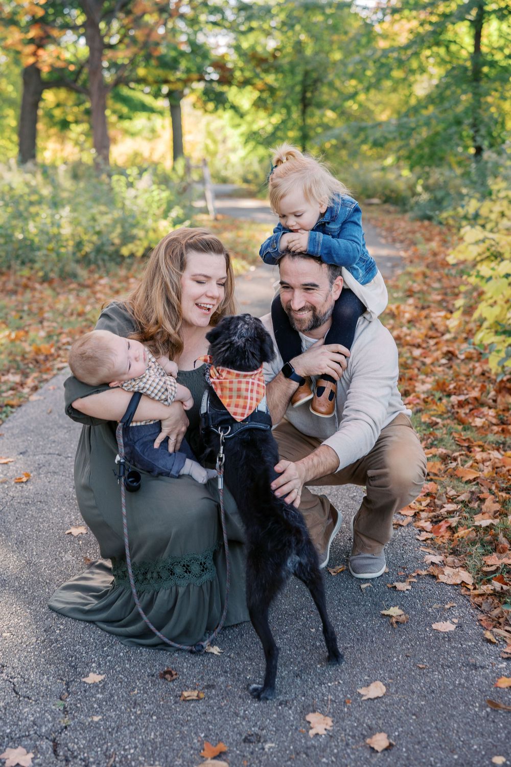 A family shares a happy moment with their black dog on an autumn path.