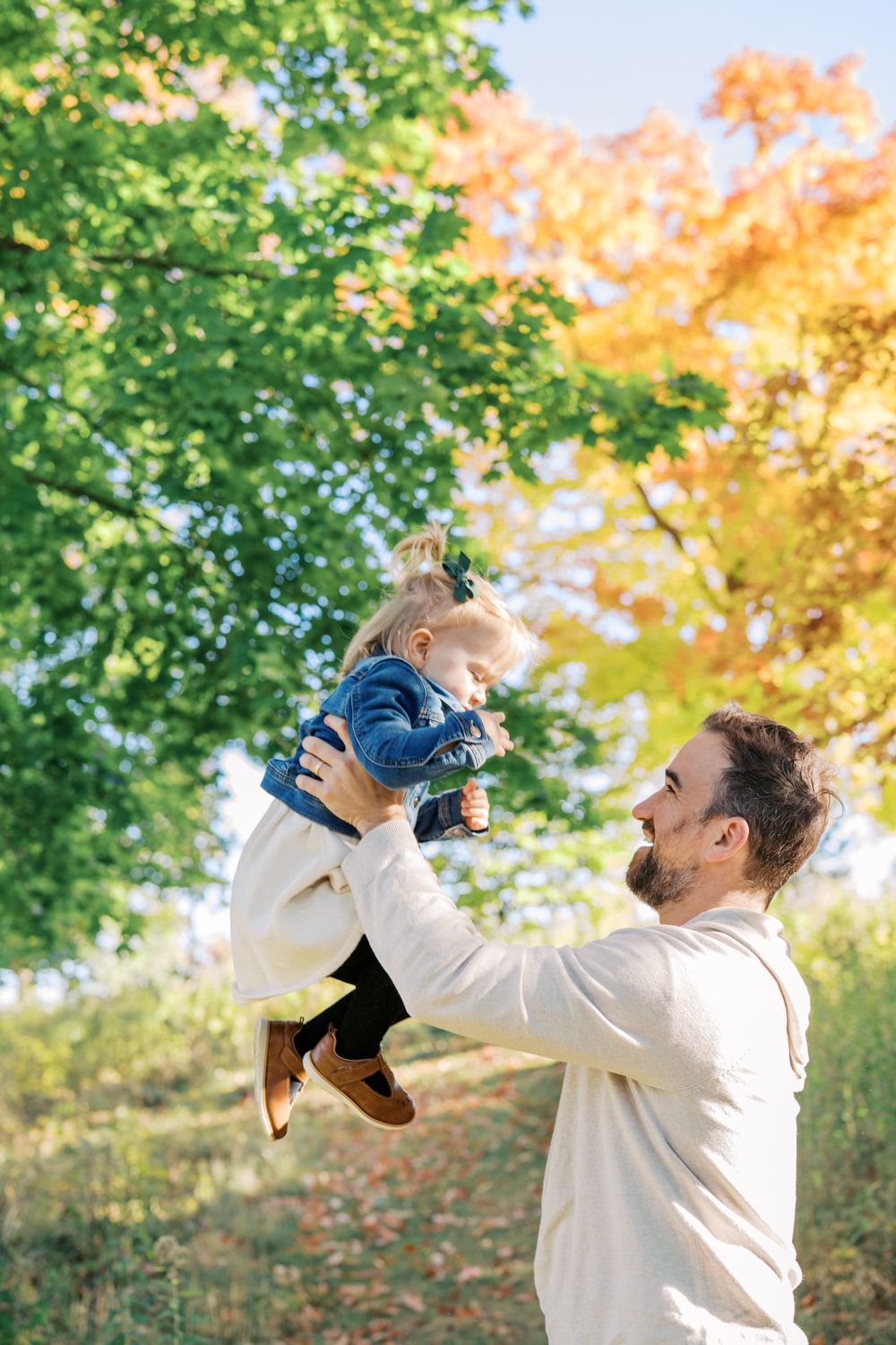 A joyful moment captured lifting a small child in the air with autumn trees in background.
