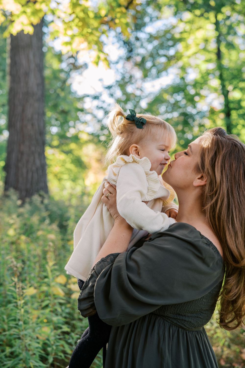 A tender moment captured in a sunlit forest setting with a black dress and cream-colored outfit.