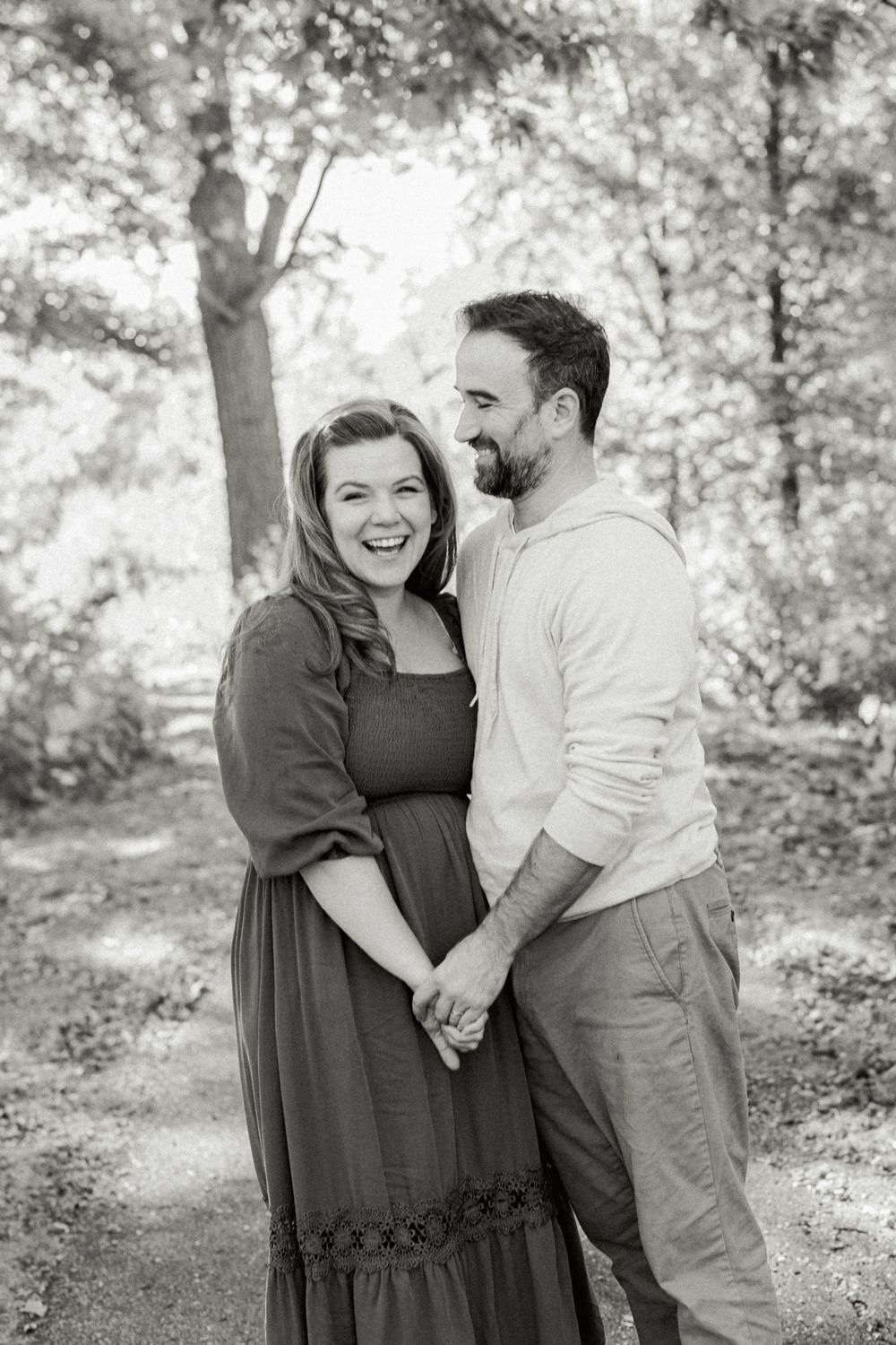 A black and white portrait of a couple sharing a romantic moment in a wooded setting.