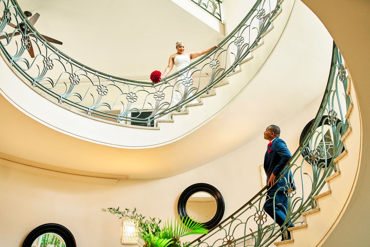Person ascending elegant spiral staircase with ornate metal railings and circular skylight.