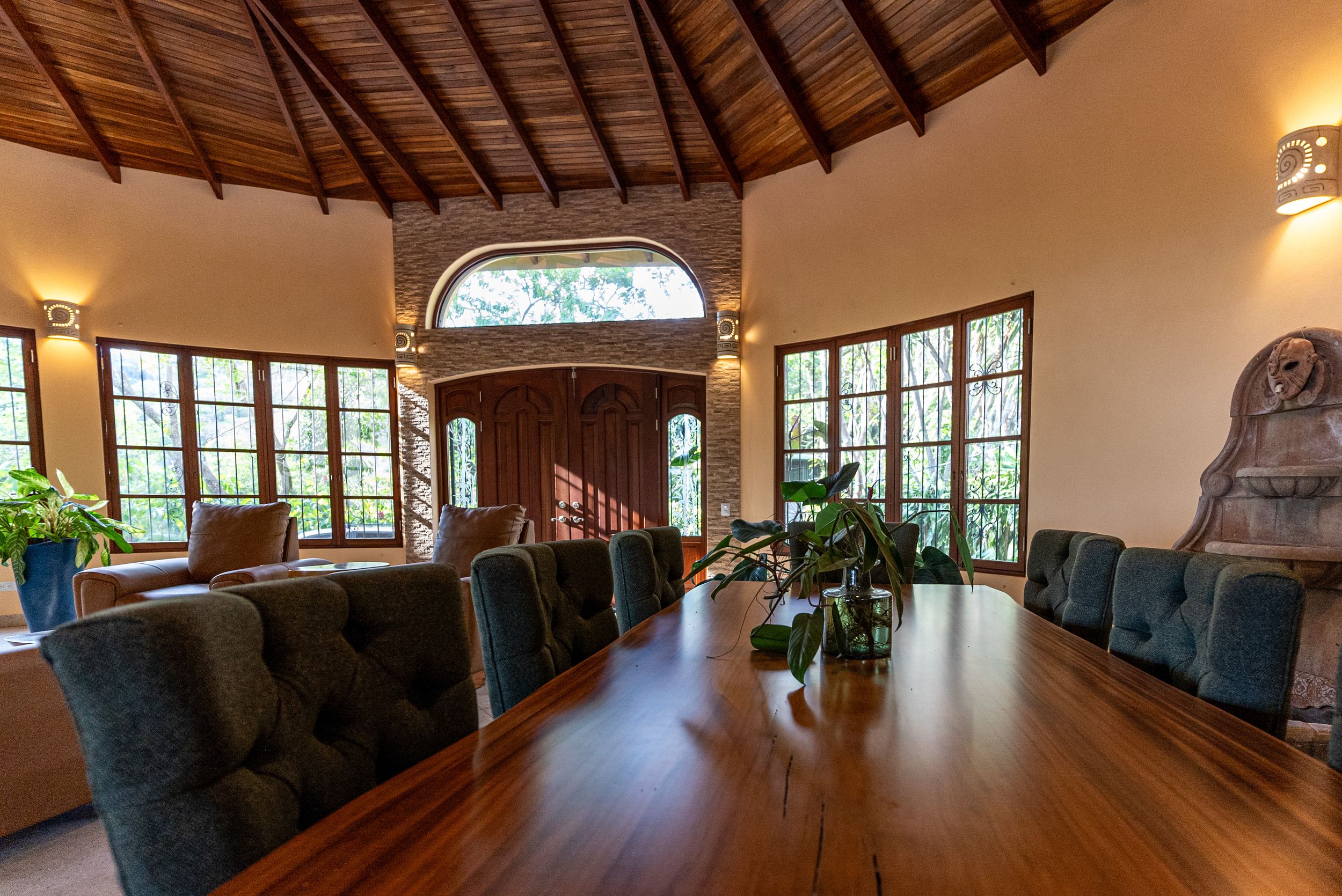 Dining area with a wooden table and upholstered chairs, surrounded by windows and natural light