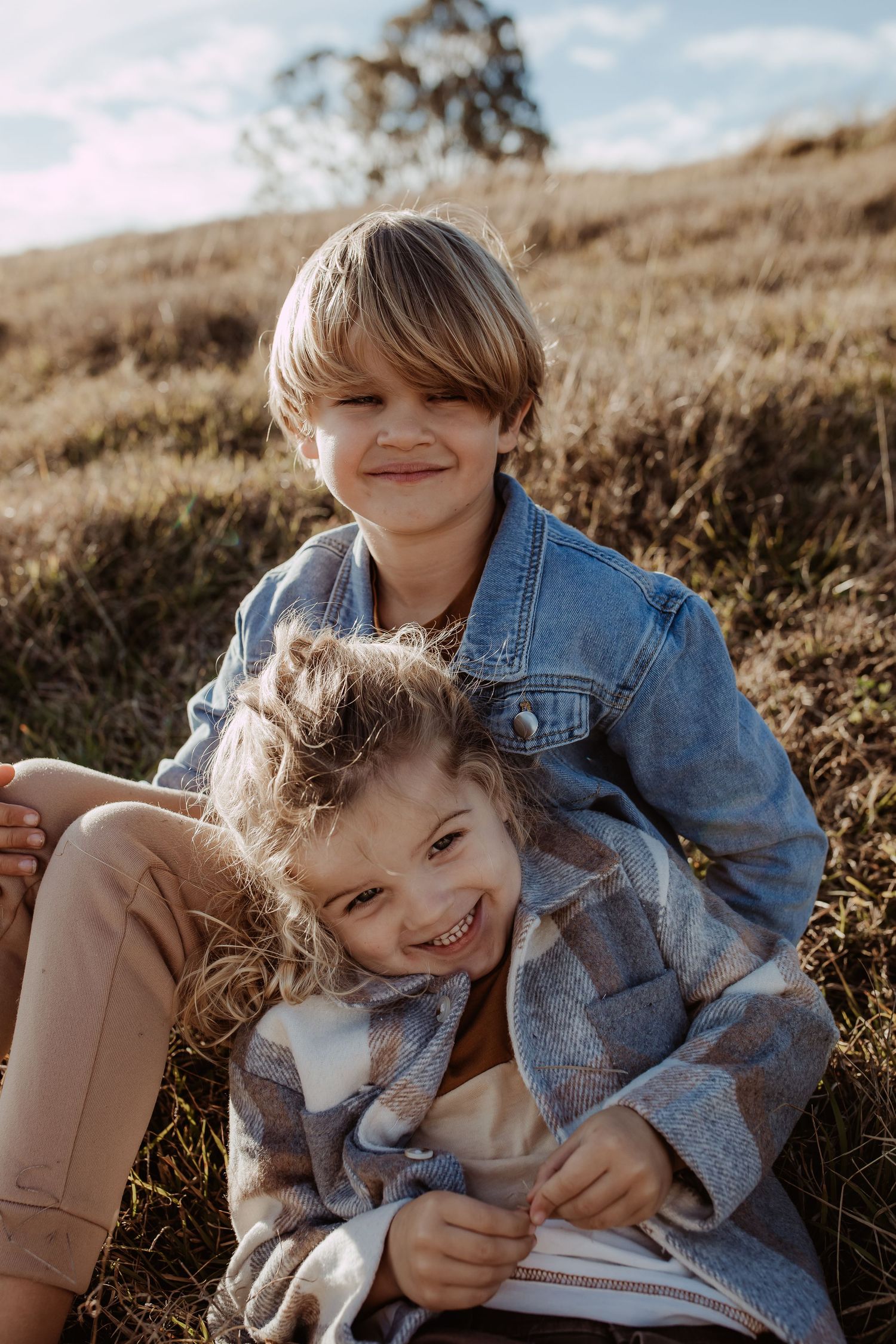 Two children in denim jackets share a joyful moment on a hillside.