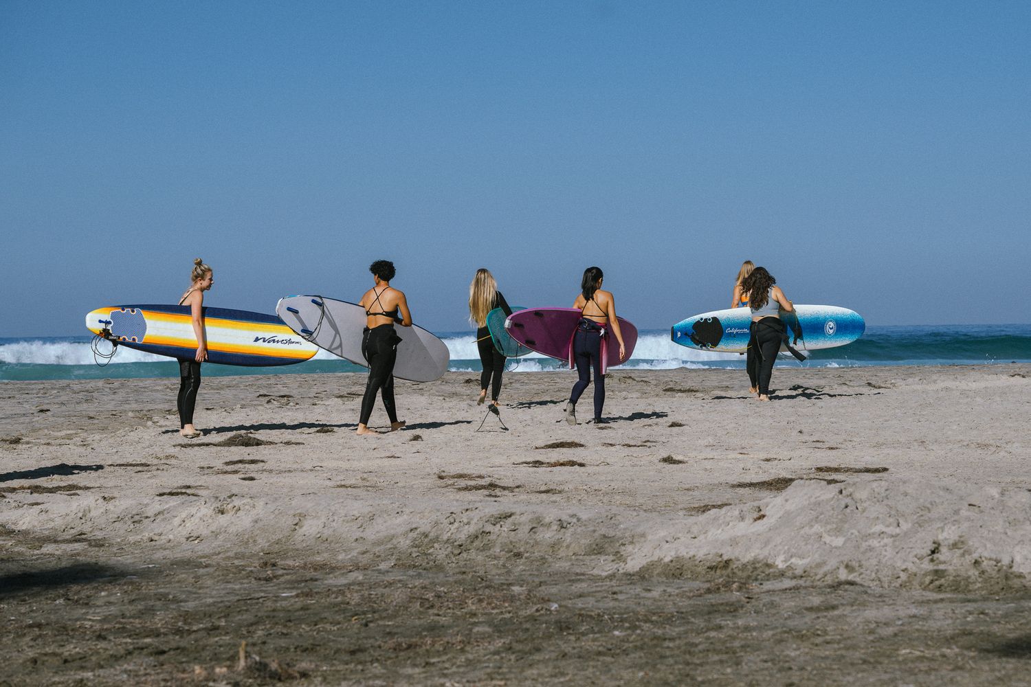 5 surfer women carrying surfboards get ready to enter the water