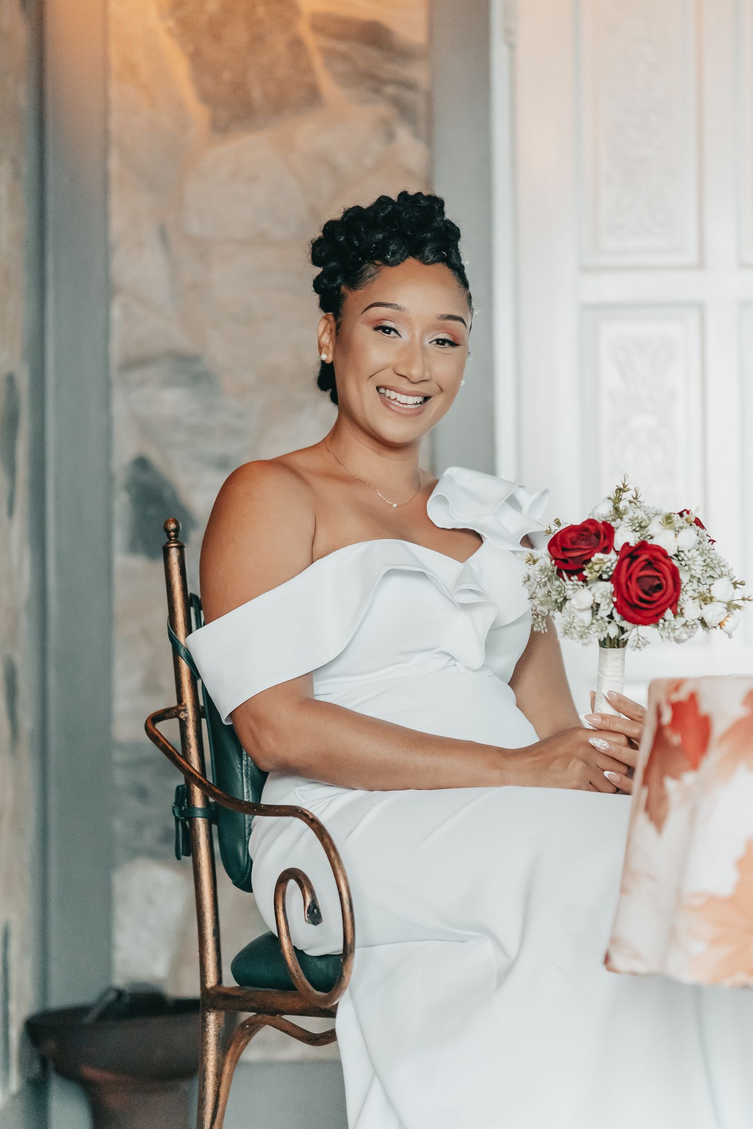 Elegant bride in off-shoulder dress poses with red and white rose bouquet.