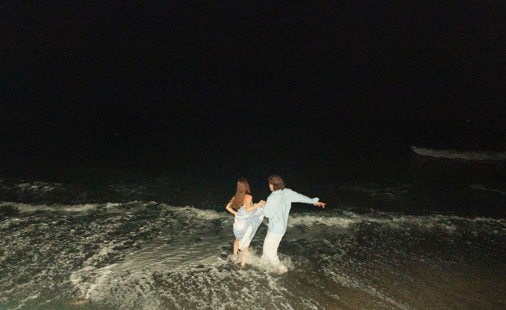 Two people playing in ocean waves at night under dark sky.