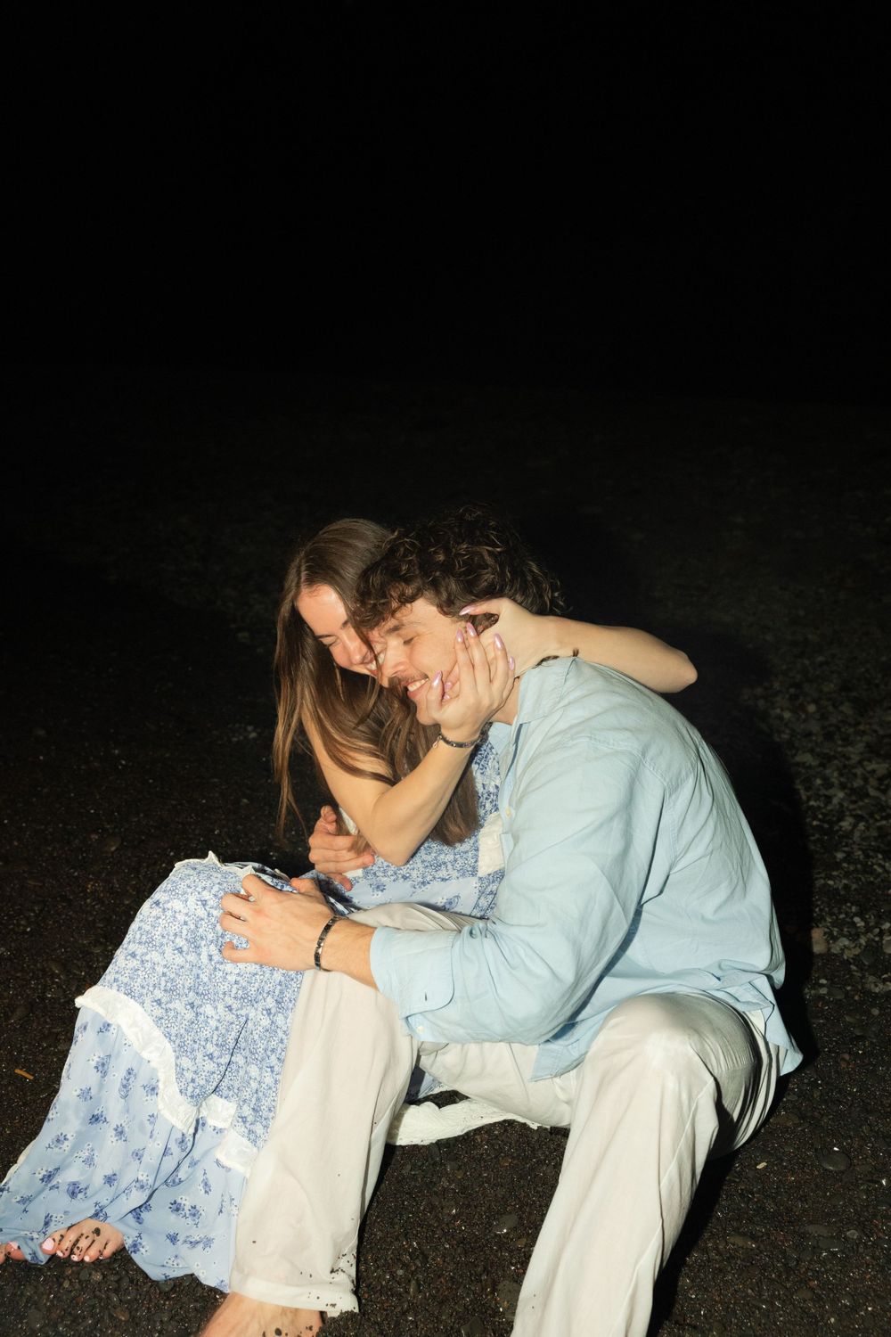 Young couple in casual clothing sitting together outdoors at night while looking at a mobile phone.
