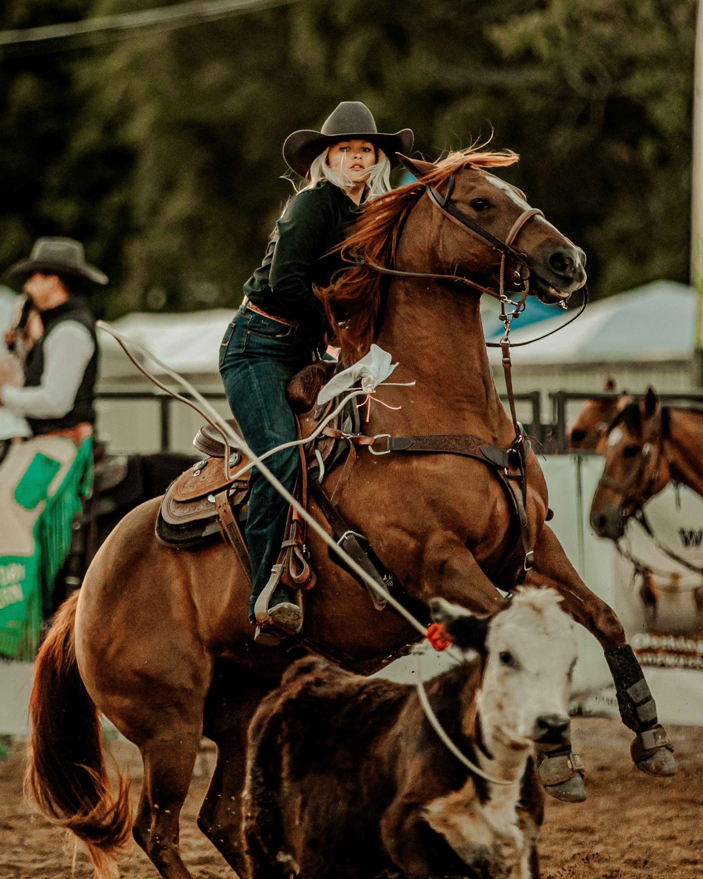 Cowgirl in western attire riding a brown horse during a rodeo competition in an outdoor arena.