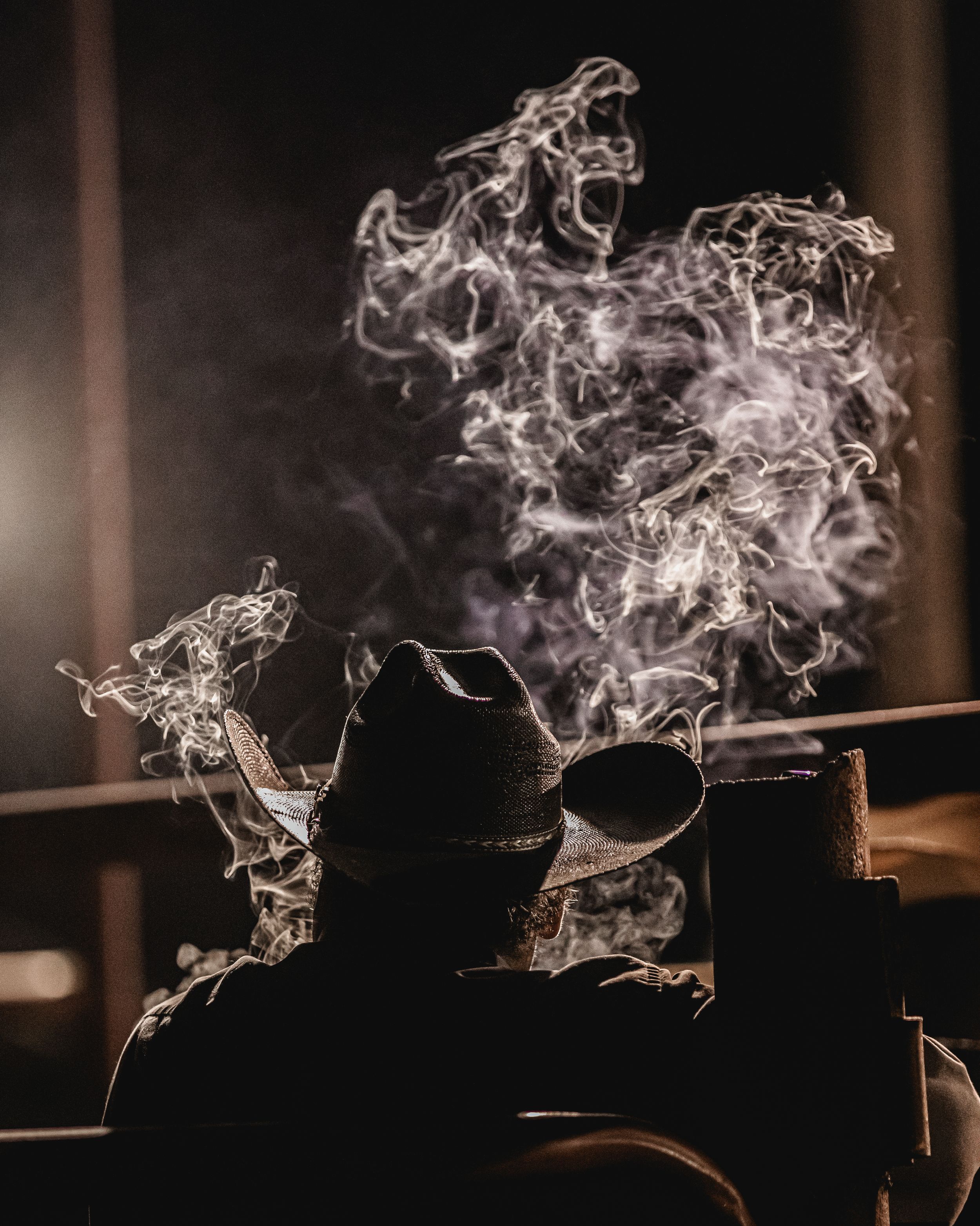Silhouetted figure in a hat with dramatic swirling smoke rising against dark background creating an atmospheric mood.