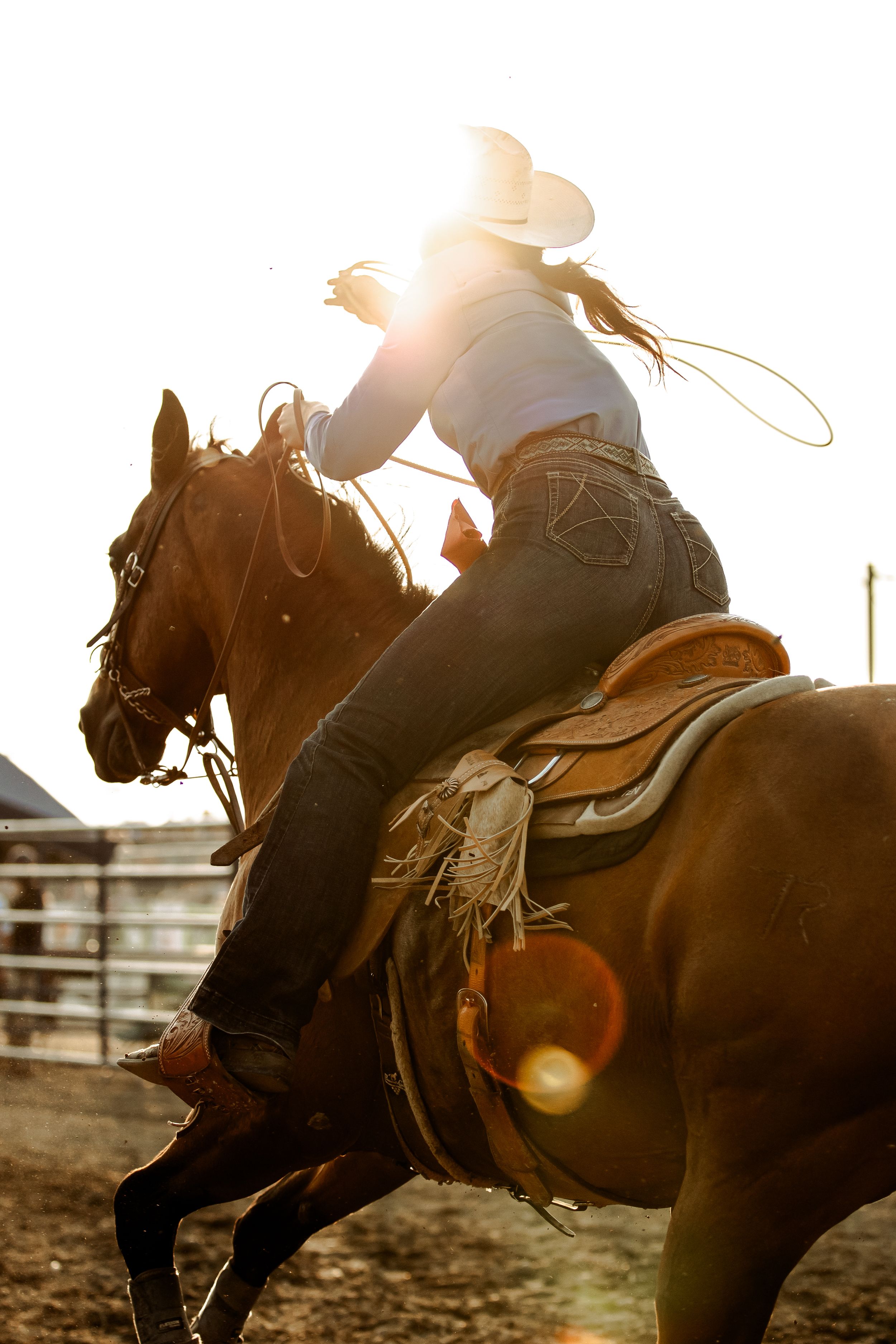 Silhouette of rodeo riders on horseback against a dramatic sunset at a western arena.