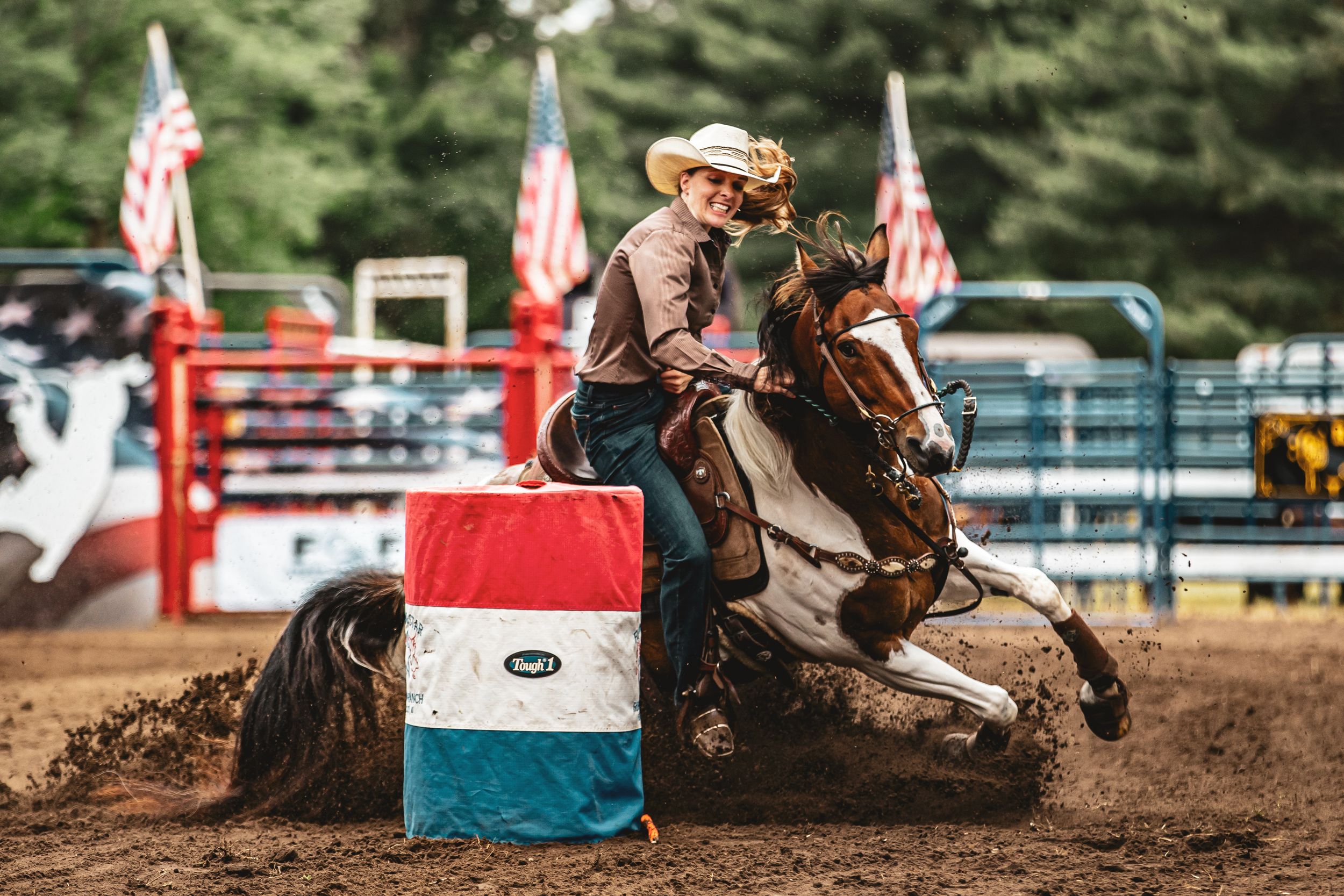 A rider on horseback competes in barrel racing at a rodeo with American flags in the background.