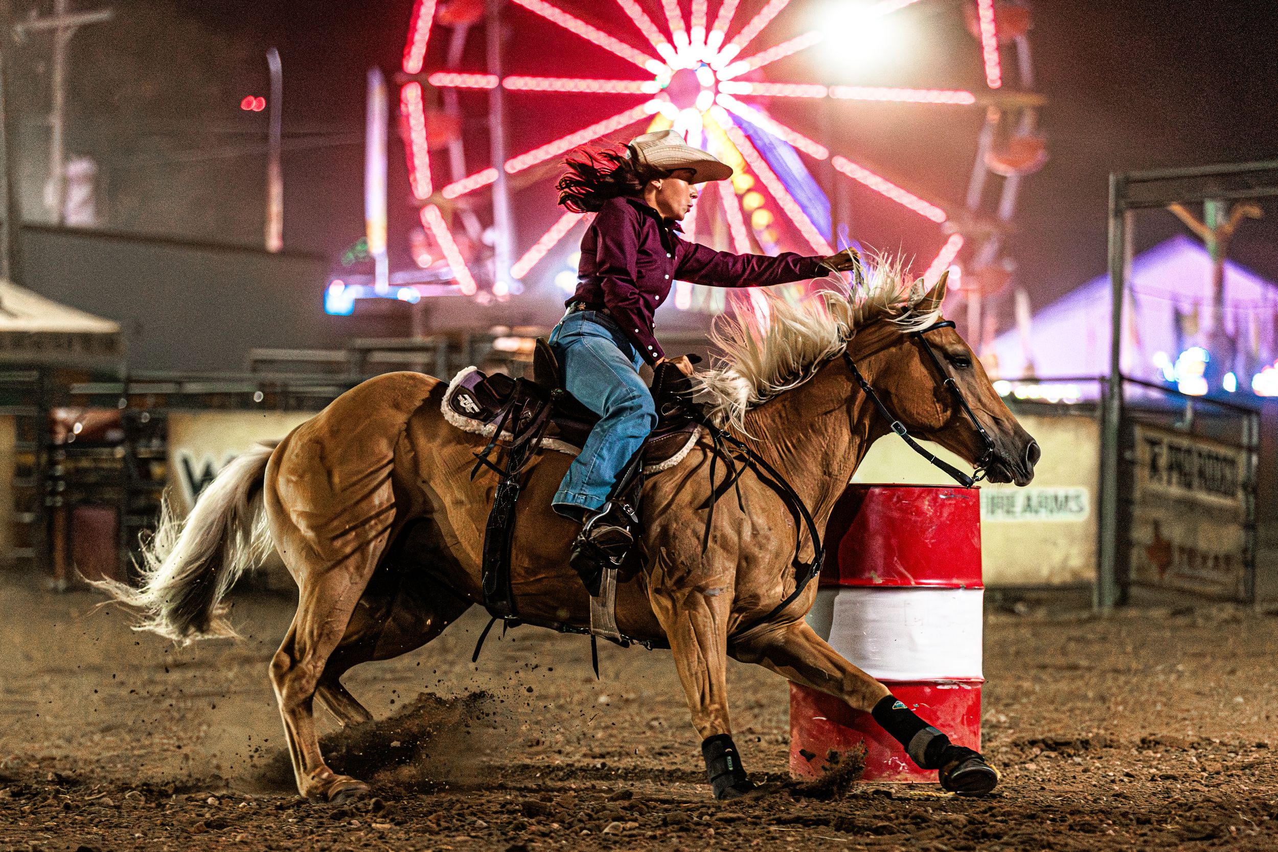 Rodeo barrel racing action shot at night with bright red neon lights illuminating the arena.