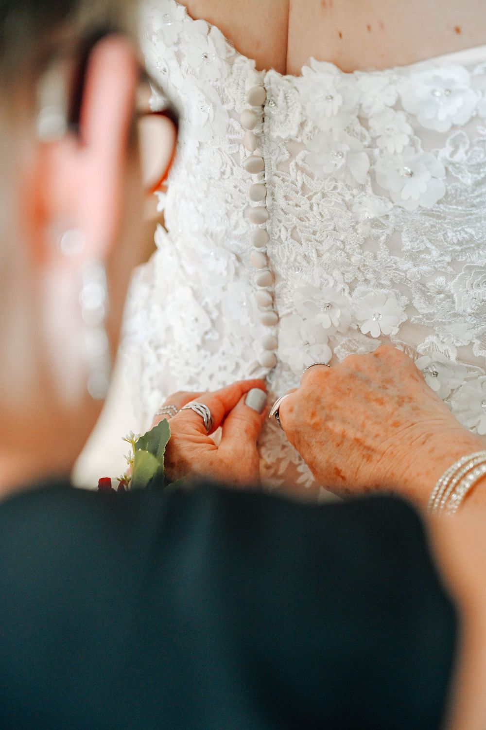 Close-up view of delicate lace details being adjusted on a white wedding dress with intricate floral embroidery.