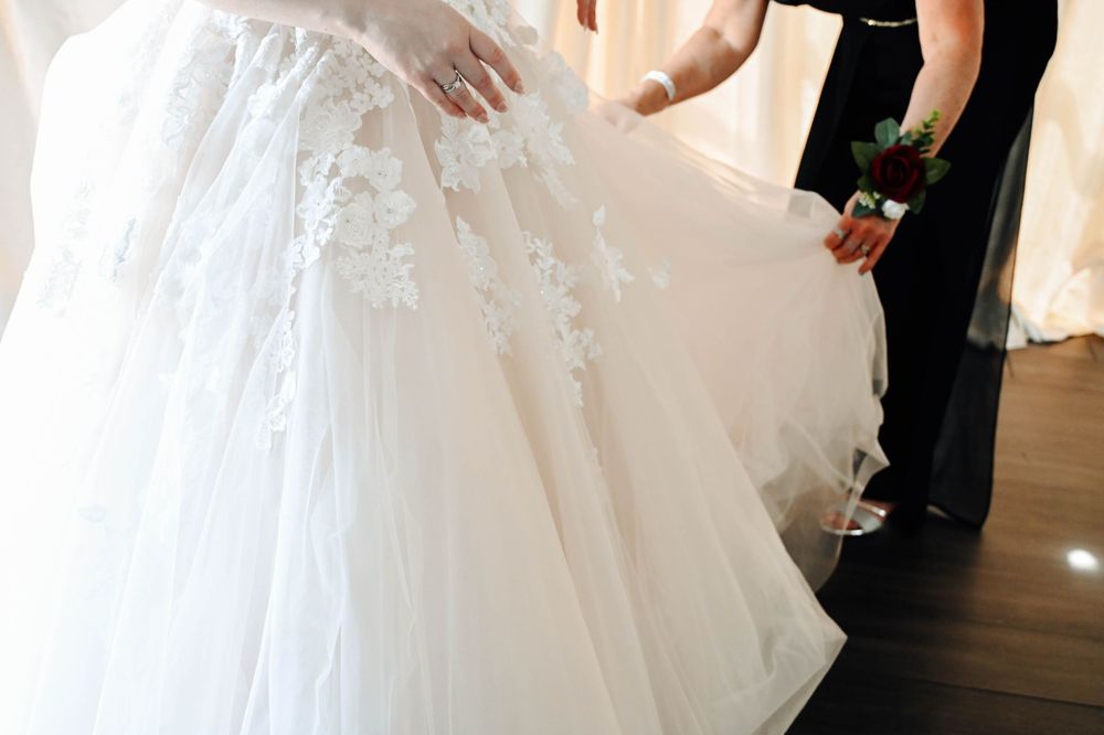 Someone adjusts the layers of a flowing white wedding dress with delicate lace details in a bridal shop.