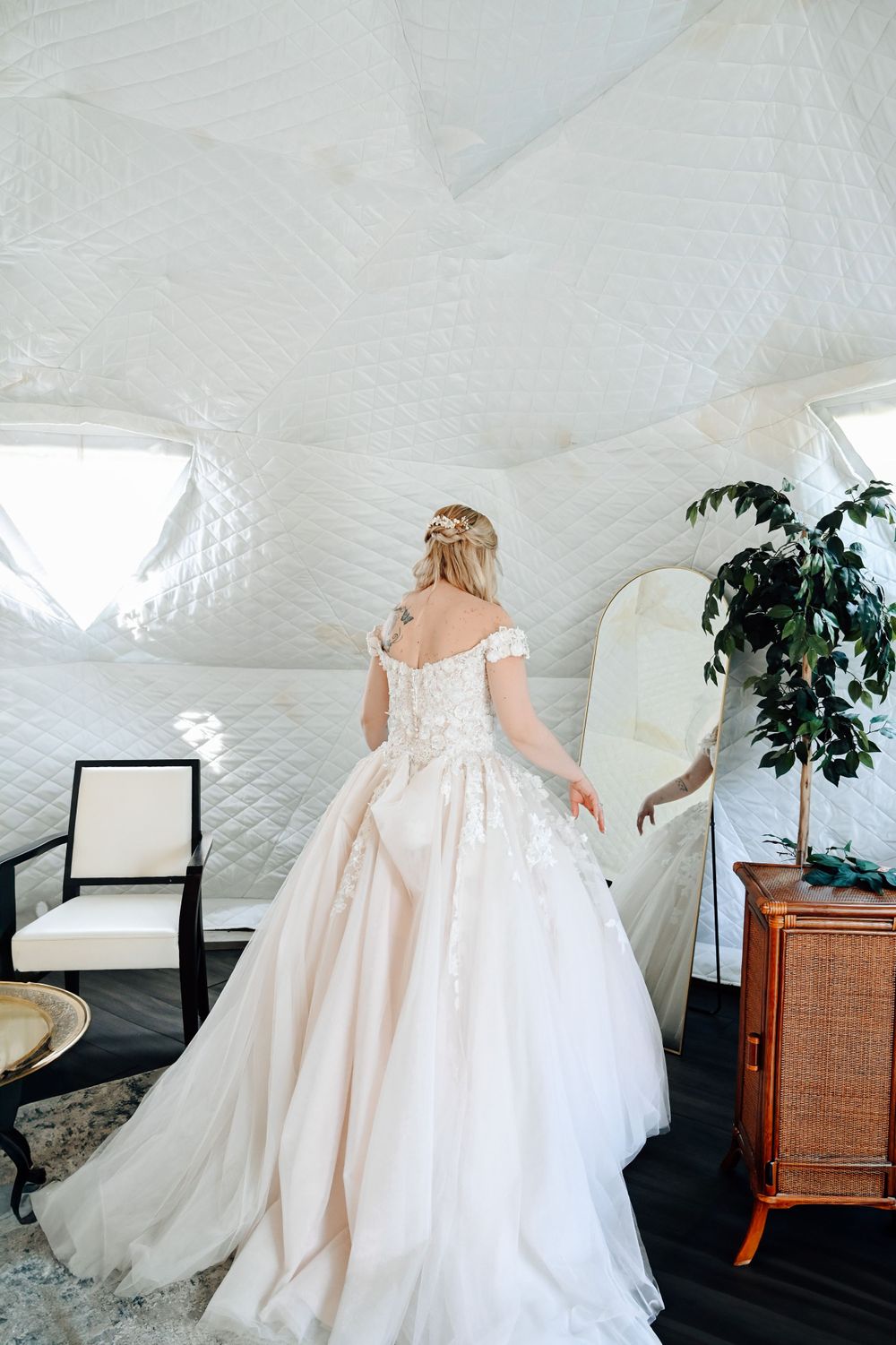 Back view of an off-shoulder princess ball gown wedding dress with lace-up corset in a bright white room.