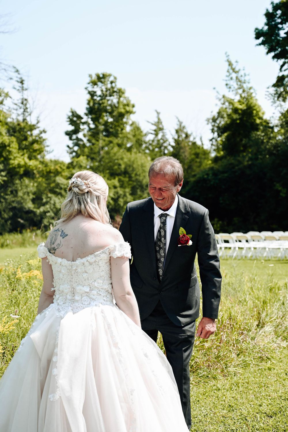 A beautiful outdoor wedding scene with white chairs set up on grass and trees in the background.