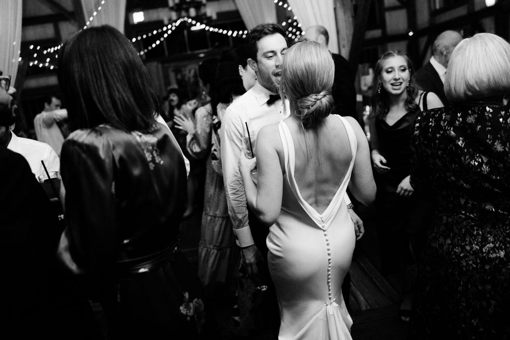 Elegant wedding guests mingle at an evening reception, with a striking backless white gown in focus.