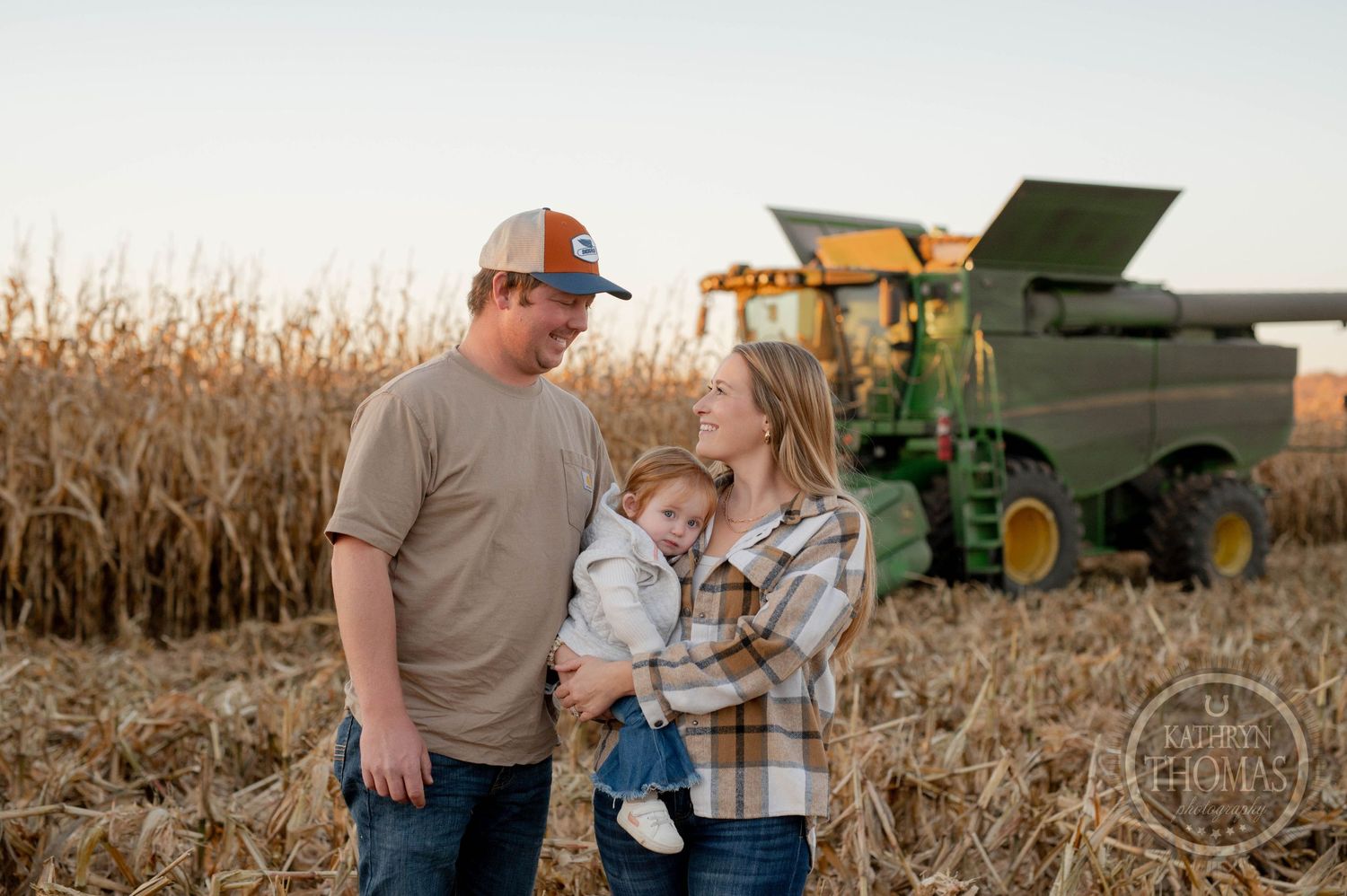 Family shares tender moment together by combine harvester in autumn cornfield.