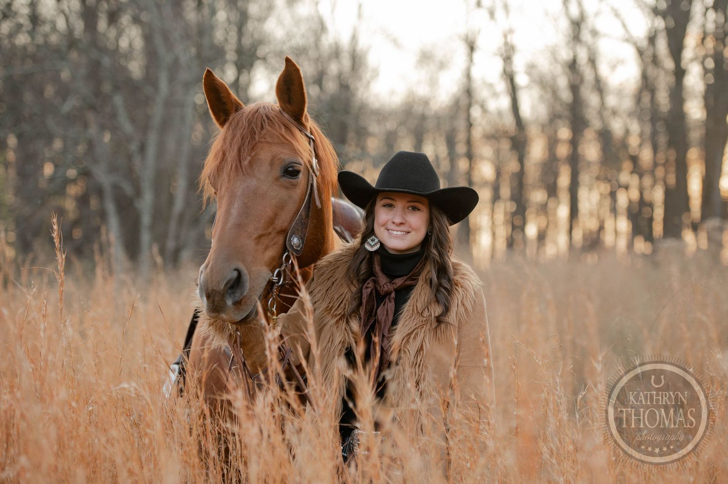 A horse and rider stand in golden grass with bare trees silhouetted in the background.