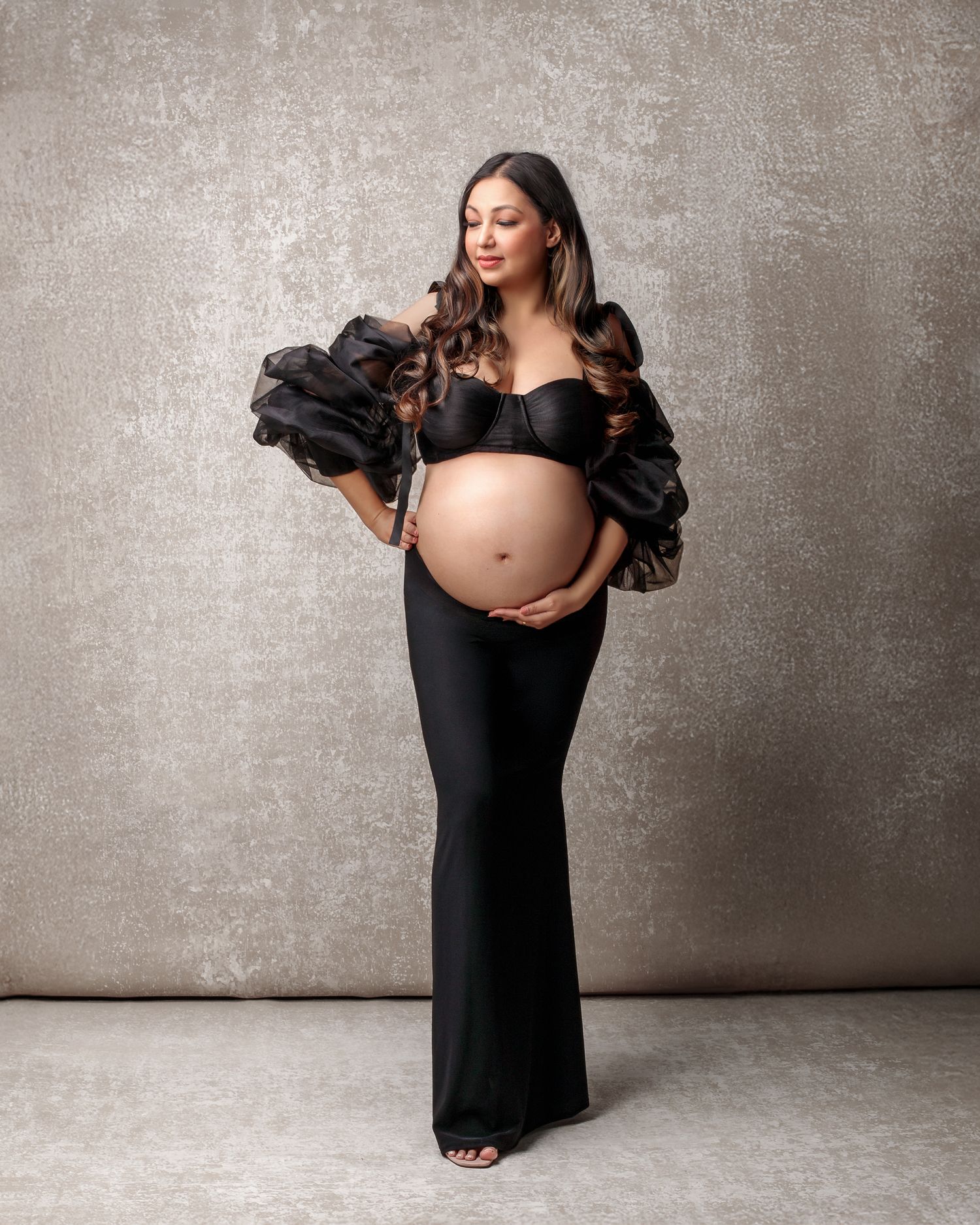 Sydney fine art maternity: mum in a black skirt and blouse, serene expression, soft lighting against hand painted backdrop.