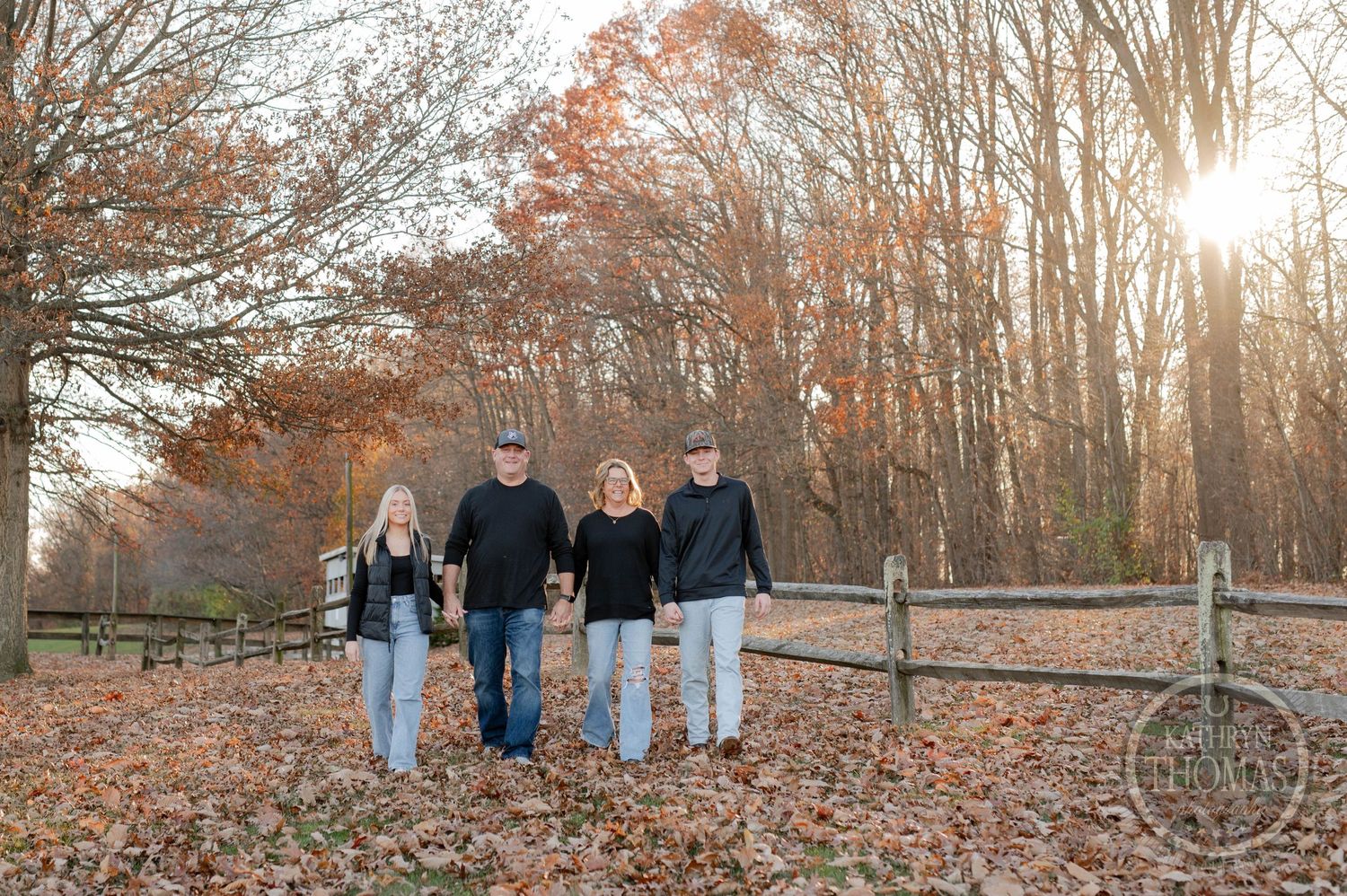 Group strolls together along rustic fence during golden hour in fall forest setting.