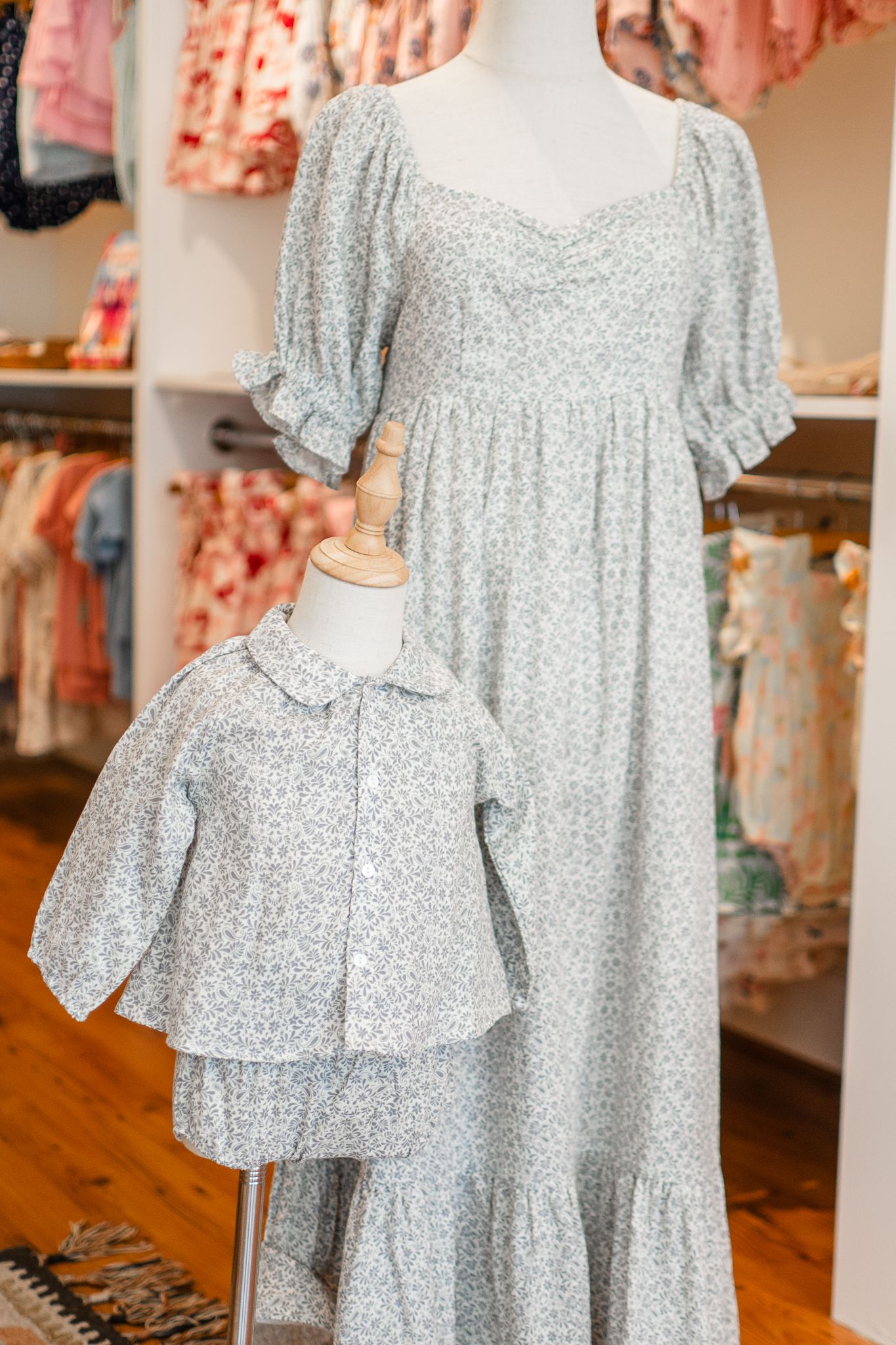Matching floral printed gray dress and childrens top displayed in boutique setting with ruffled details and puff sleeves.