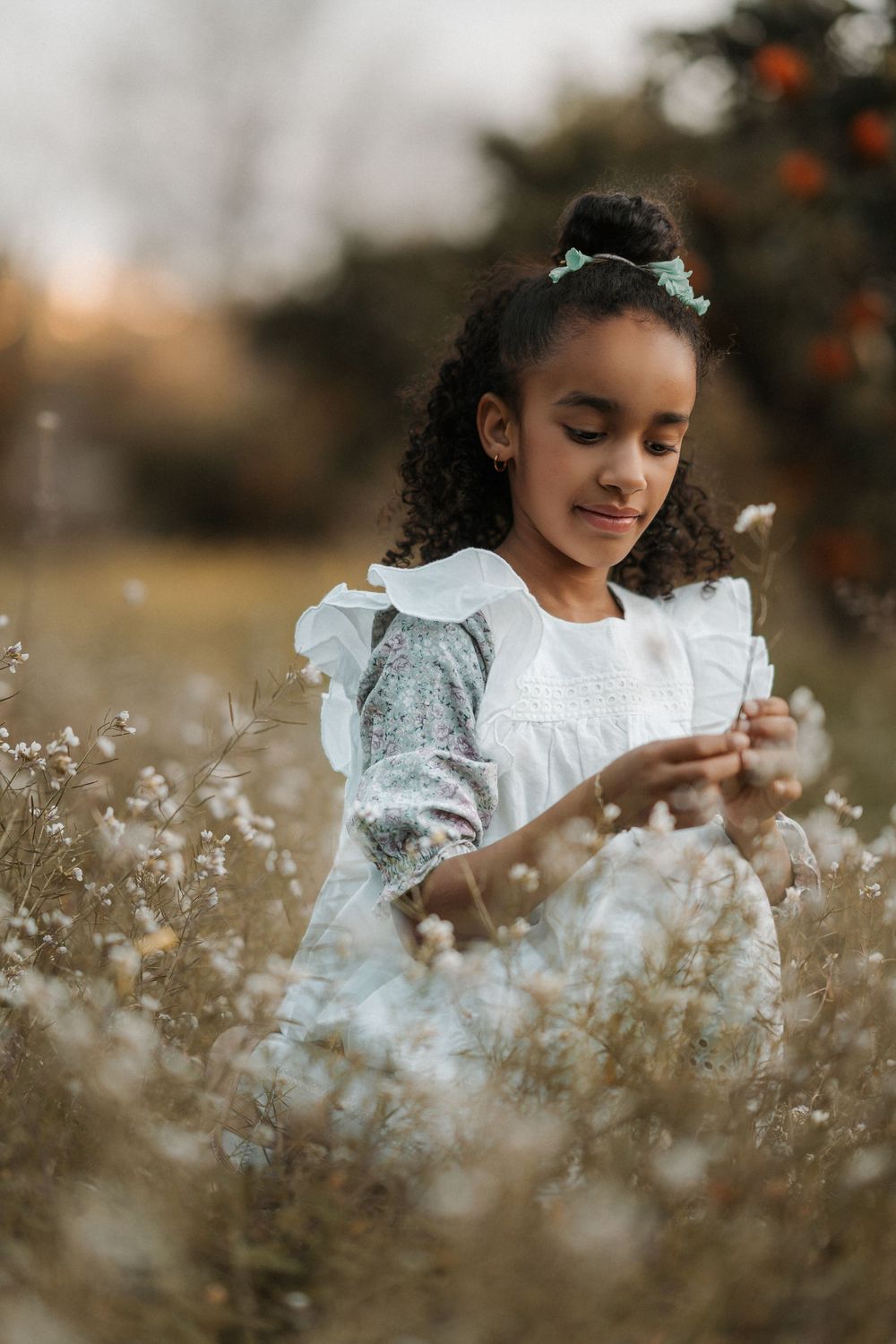 A child in a white dress gathers delicate dandelion seeds in a dreamy autumn field at golden hour.