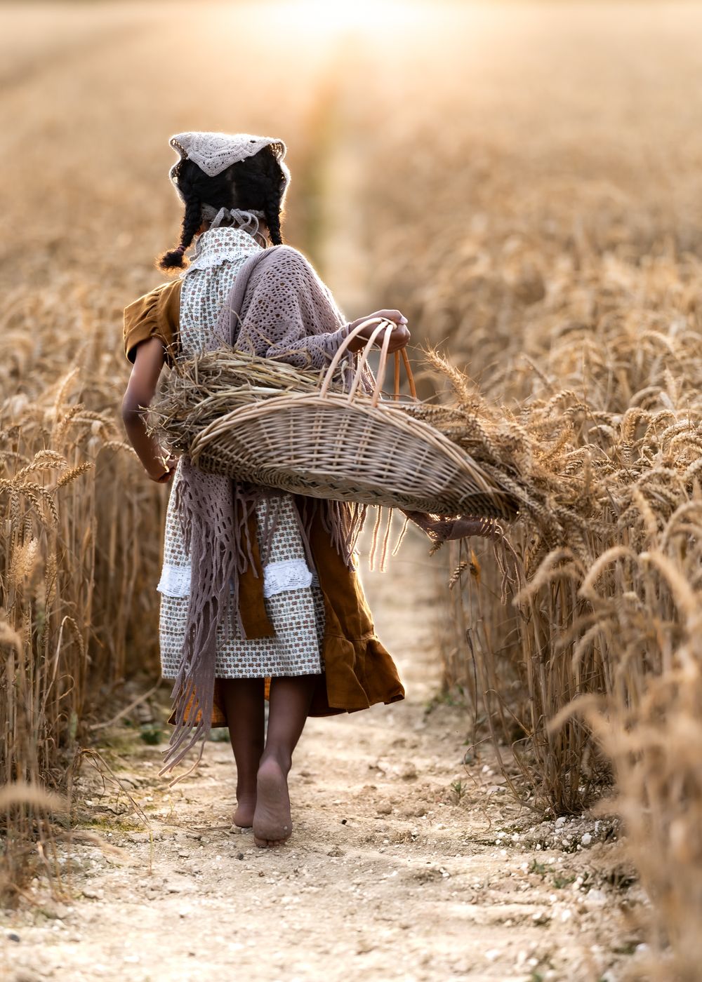 Figure carrying wicker basket walking through golden wheat field at sunset.