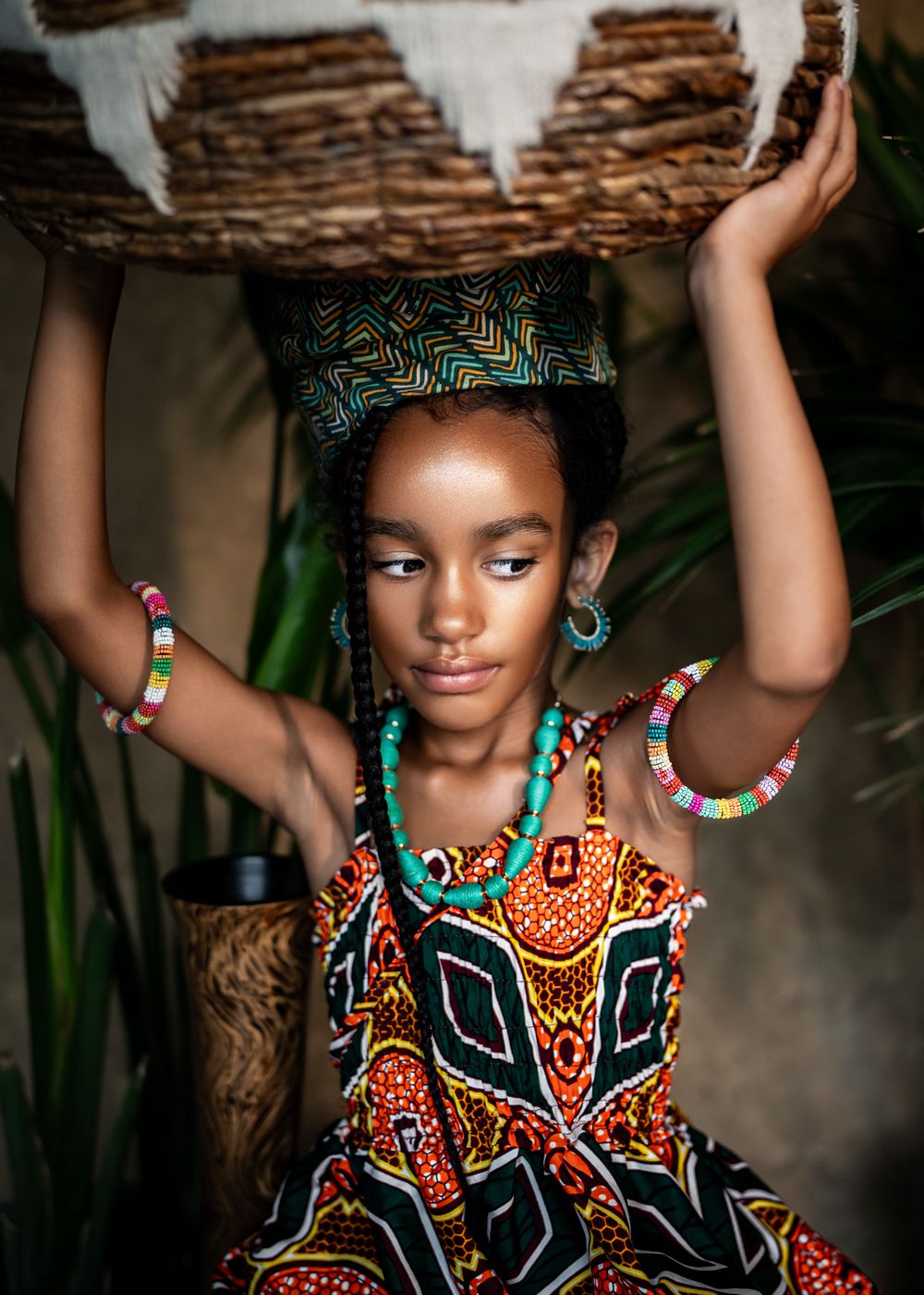 Traditional African-inspired fashion portrait with colorful beaded jewelry and patterned dress against tropical foliage background.