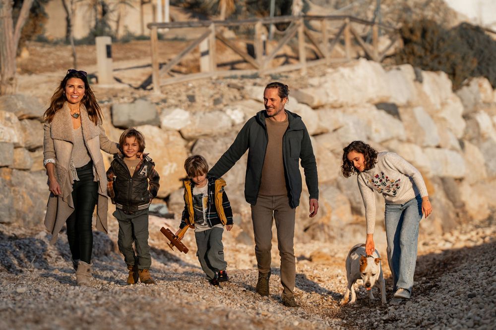 A family walks together with their two dogs along a rocky hillside during golden hour.