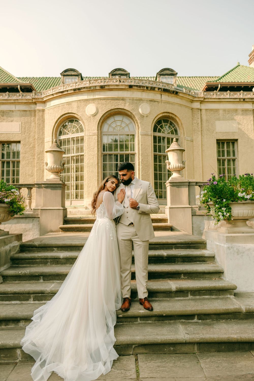 Newlywed couple shares an intimate moment on the grand stone steps of an elegant historic building with arched windows.