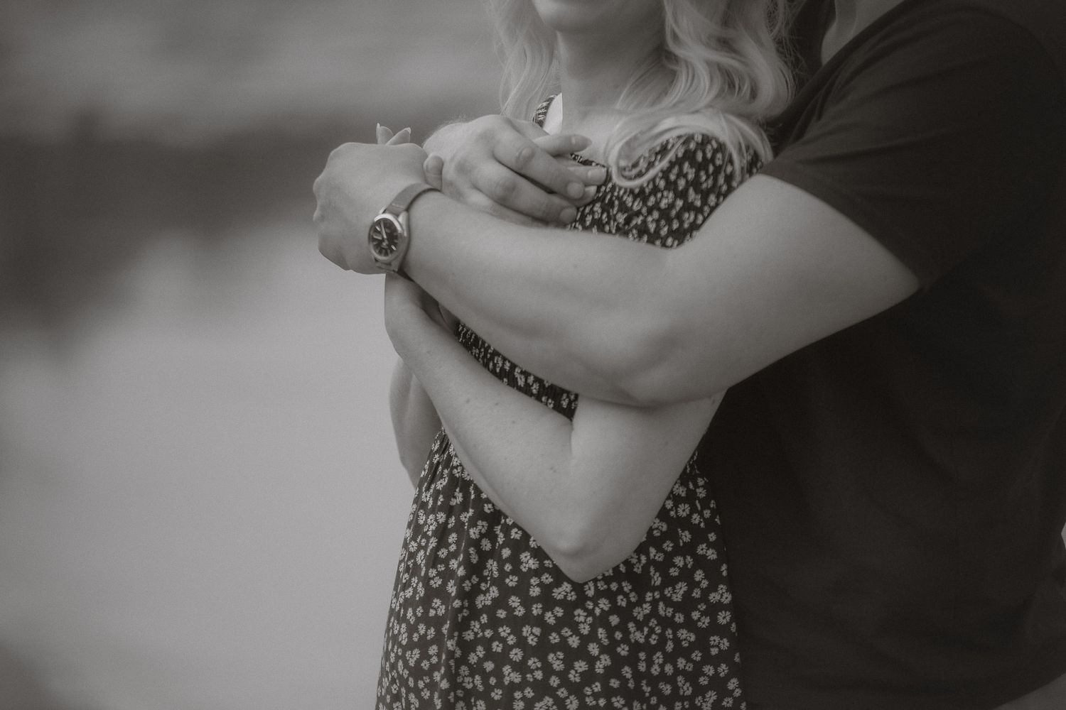 Black and white close-up of a couple embracing, with one person wearing a floral patterned dress.