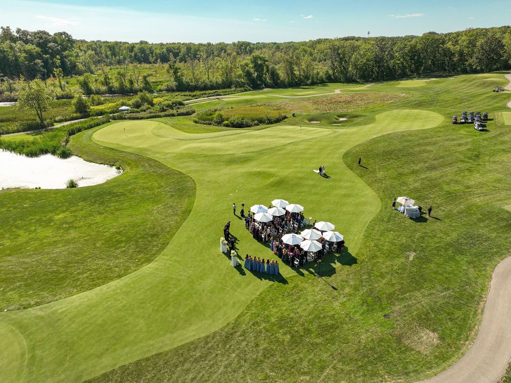 Aerial view of a golf course event with guests gathered under white umbrellas on lush green fairways.
