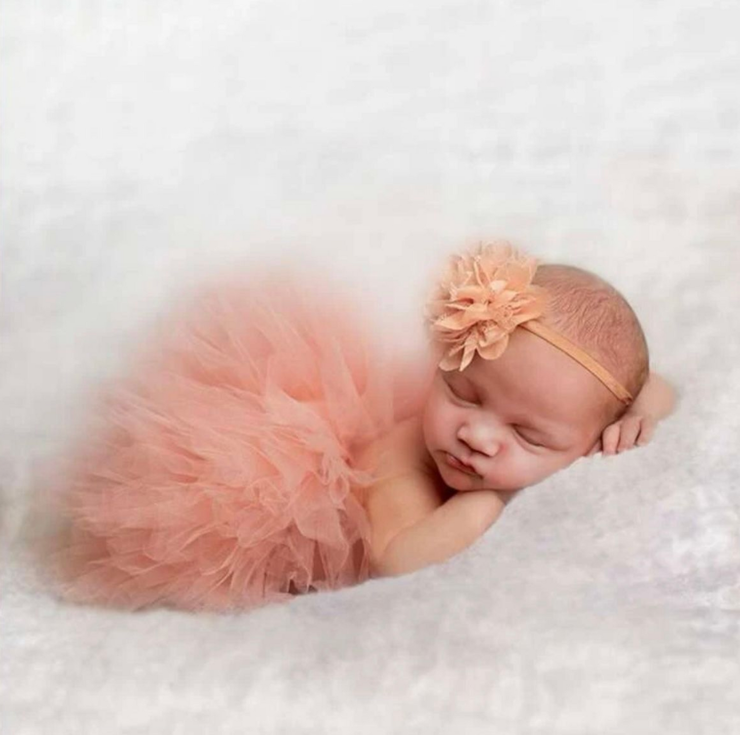 Newborn photography with peach tulle tutu on white fluffy backdrop.