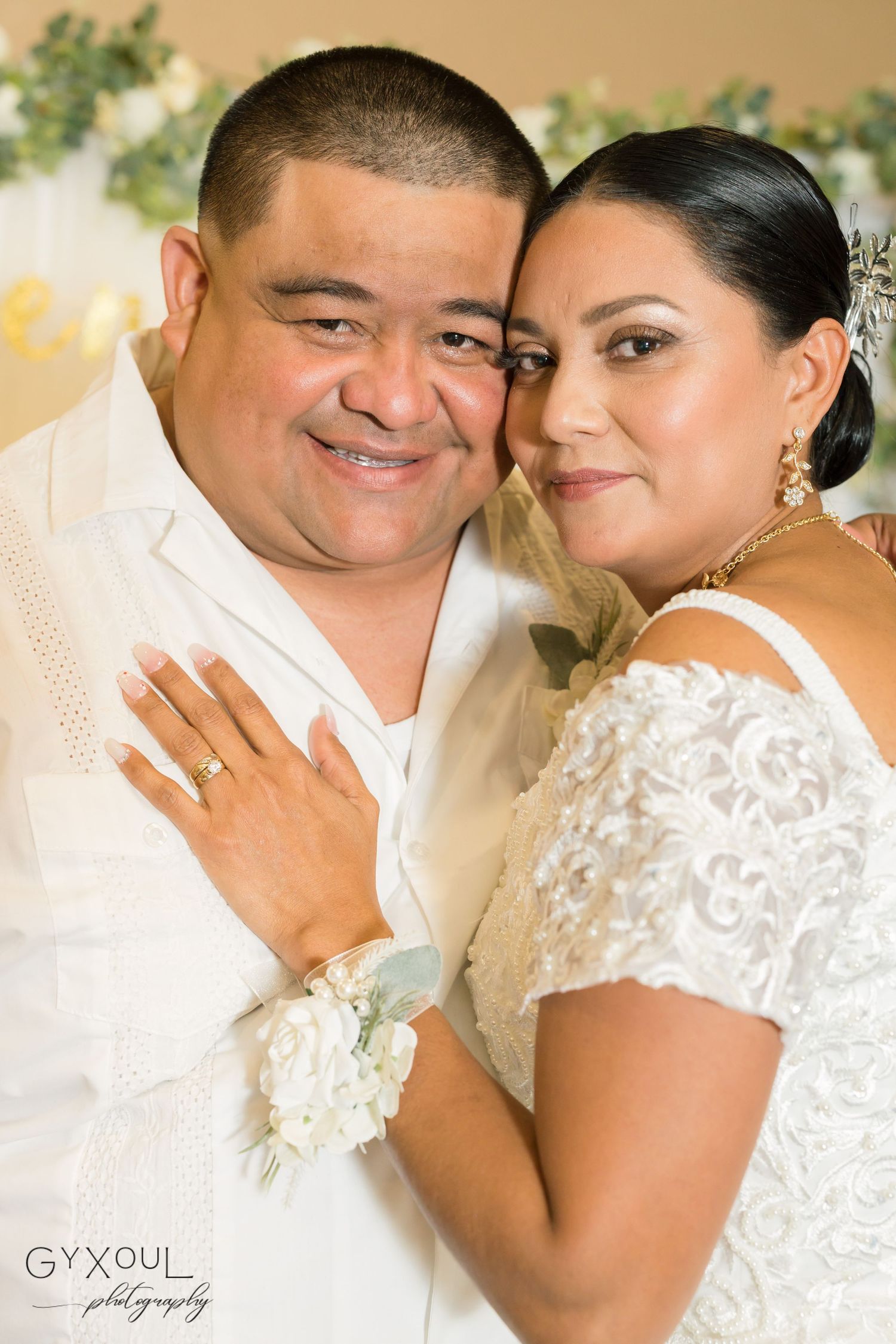 Happy newlyweds pose together in white wedding attire with floral accents.