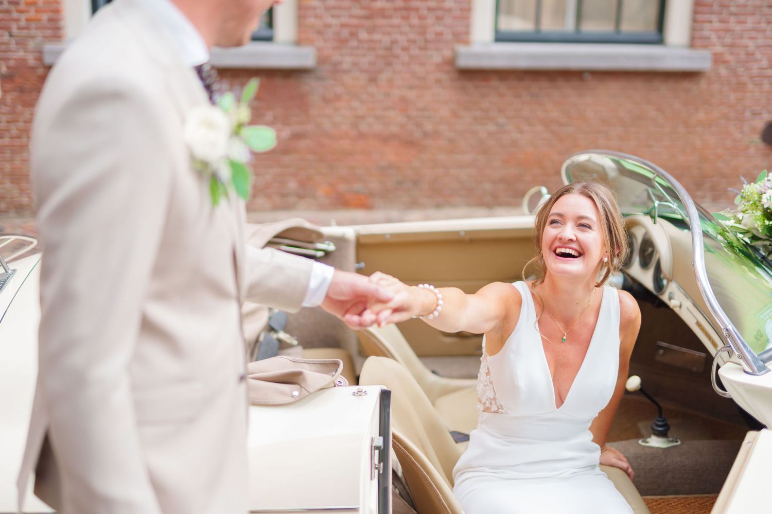 A couple holds hands during their wedding ceremony with white floral arrangements and wine barrels in the background.