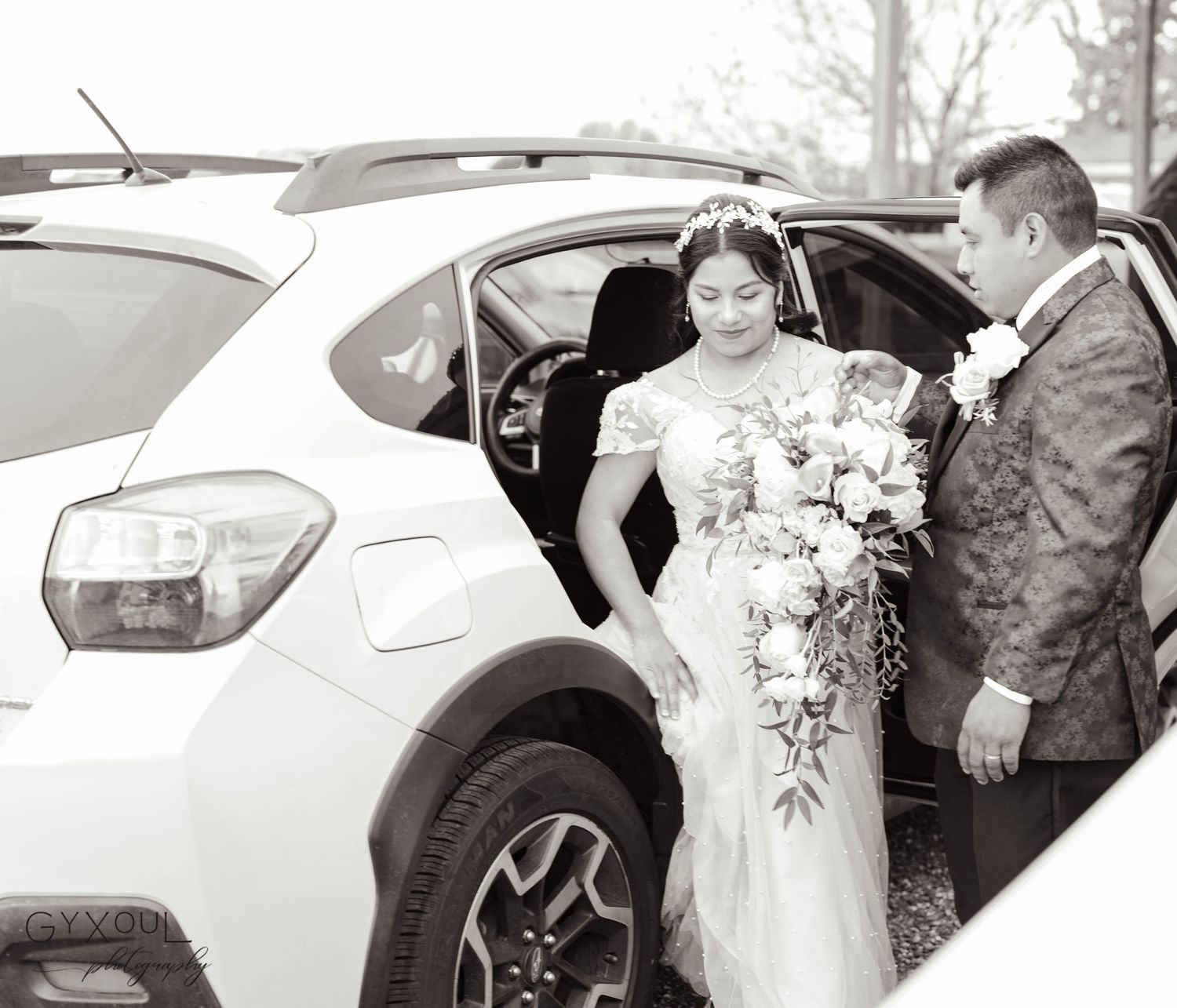 Wedding couple by white car with elegant floral bouquet and formal attire.